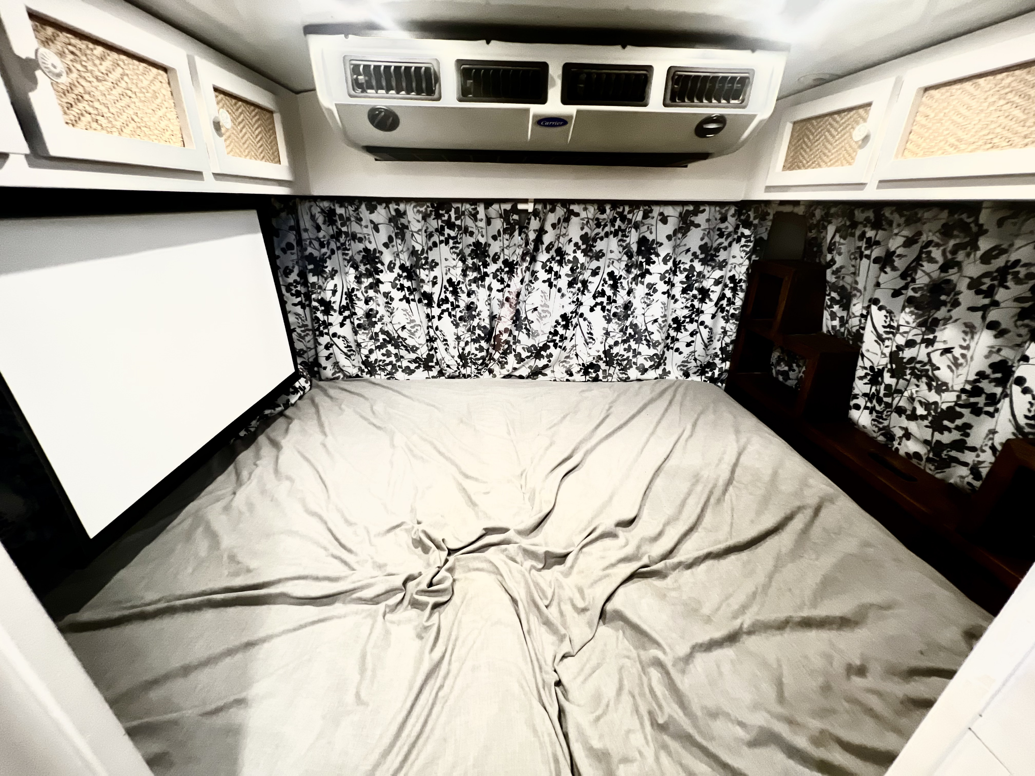 Cozy RV rental bedroom: bed, patterned curtains, woven cabinets, AC unit, and a handy projector screen.. Chevy C4500 Kodiak 2008
