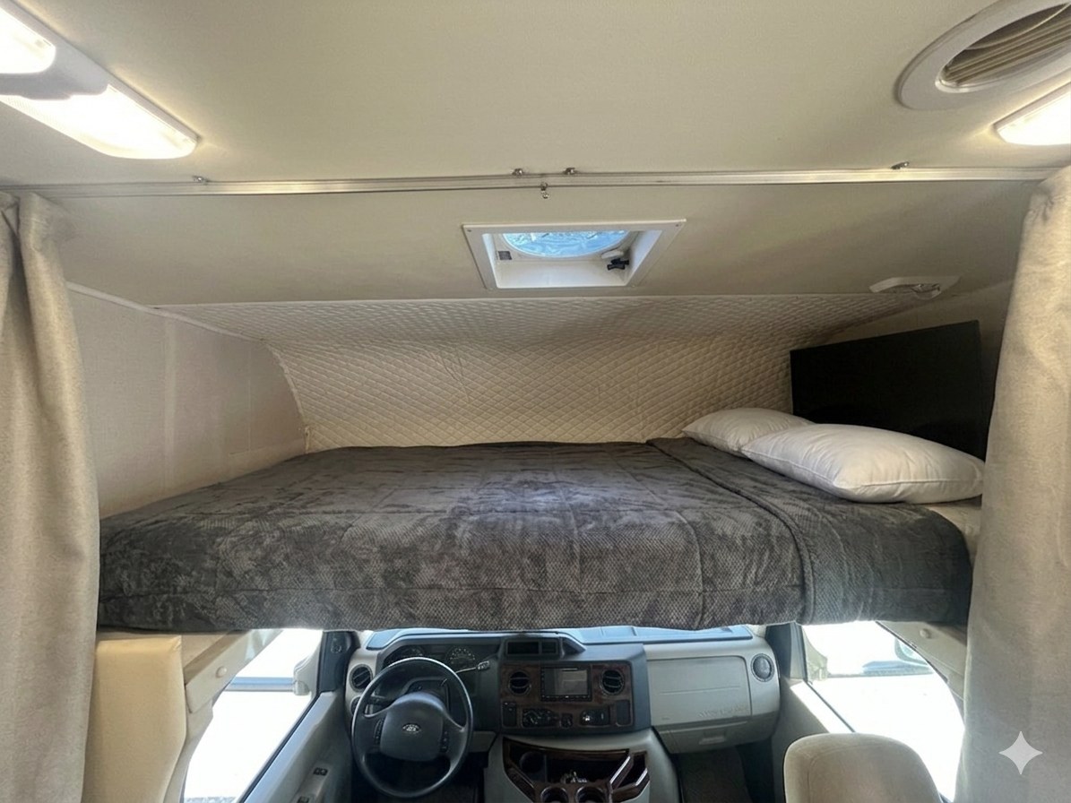 Interior view of an RV rental: a cozy over-cab bed with pillows & blanket, situated above the driver's cockpit.. Forest River Coachmen Leprechaun 2010