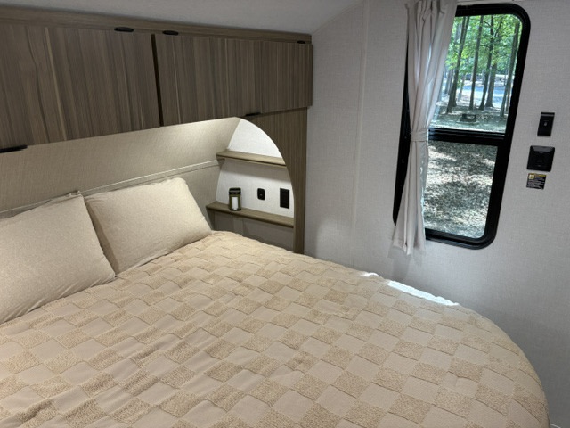 Cozy RV rental bedroom featuring a comfy bed with overhead cabinets, and a window view looking out to a wooded campground.. Forest River Salem Cruise-Lite 2026