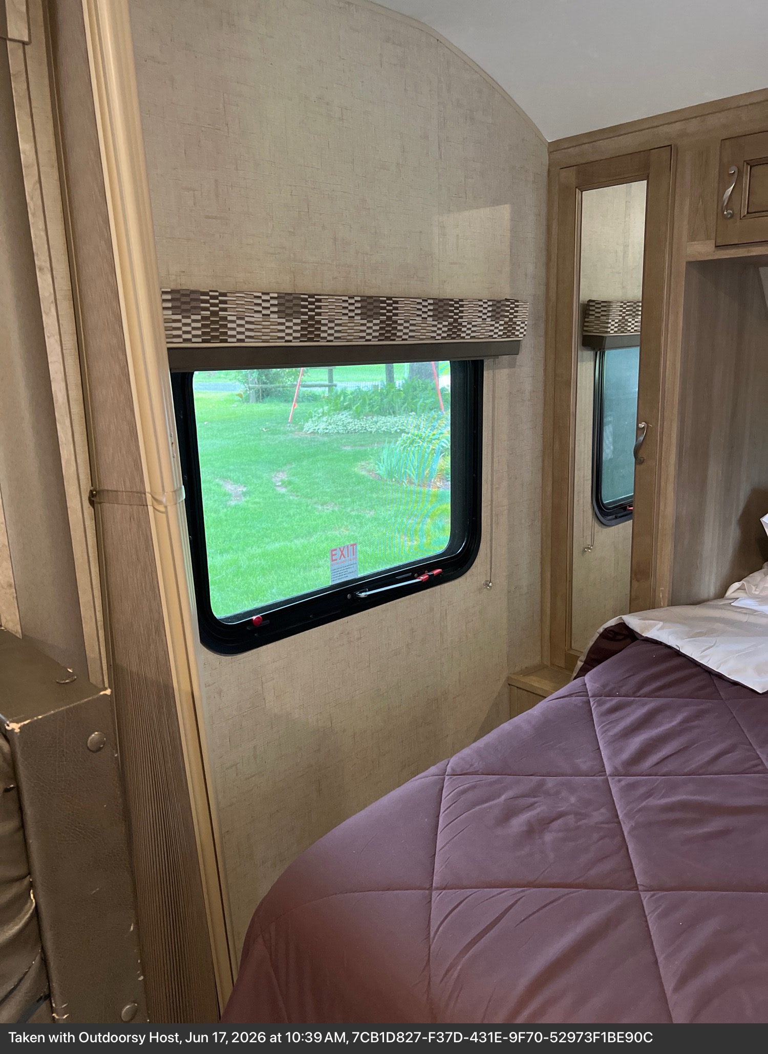 Inside an RV rental bedroom showing a purple-covered bed, mirror, and window with an 'EXIT' sign, offering a green outdoor view.. KZ VISION 2017