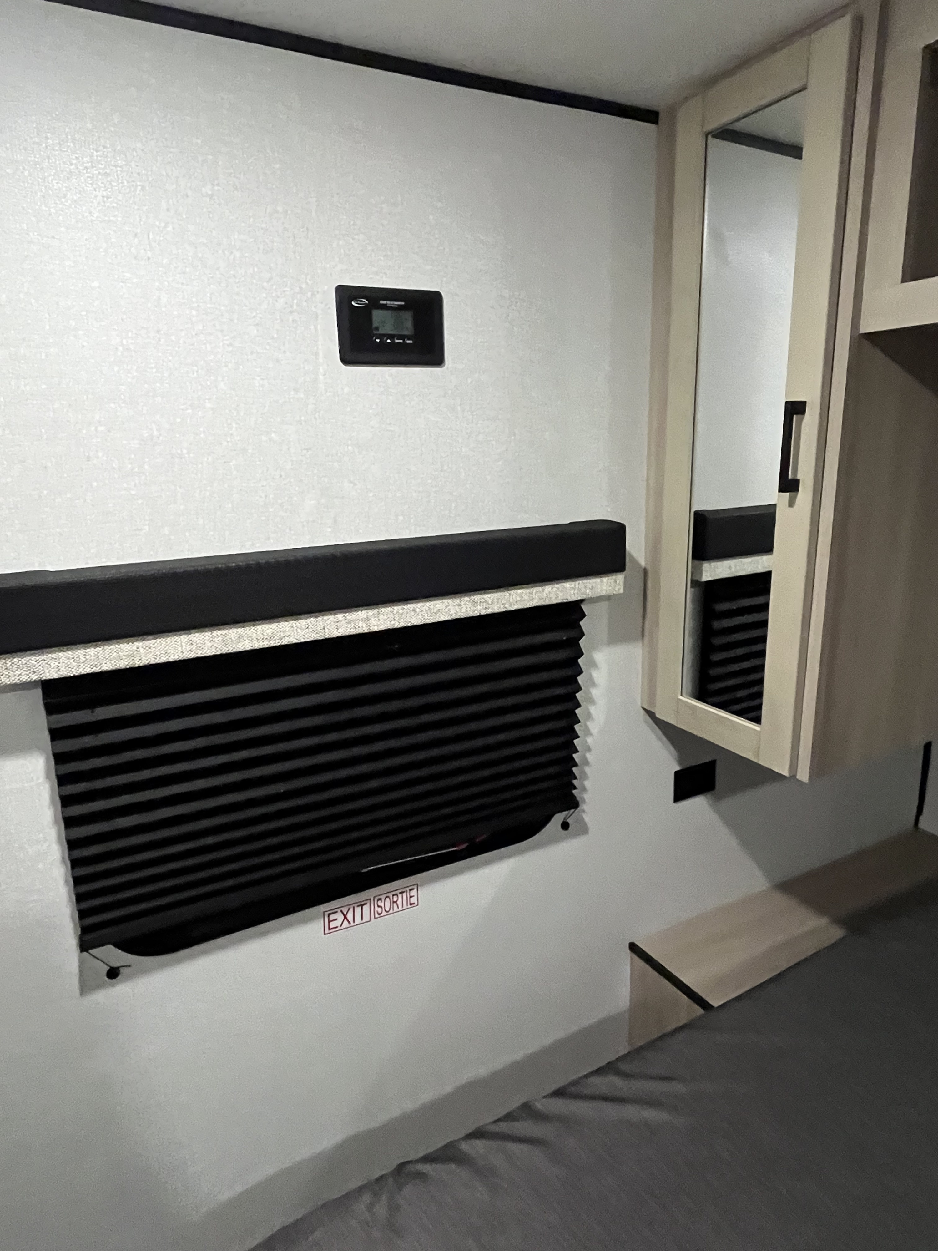 Functional RV rental interior with system control panel, pleated window blind with 'EXIT', mirrored cabinet, and comfortable bed.. Heartland TT 2026
