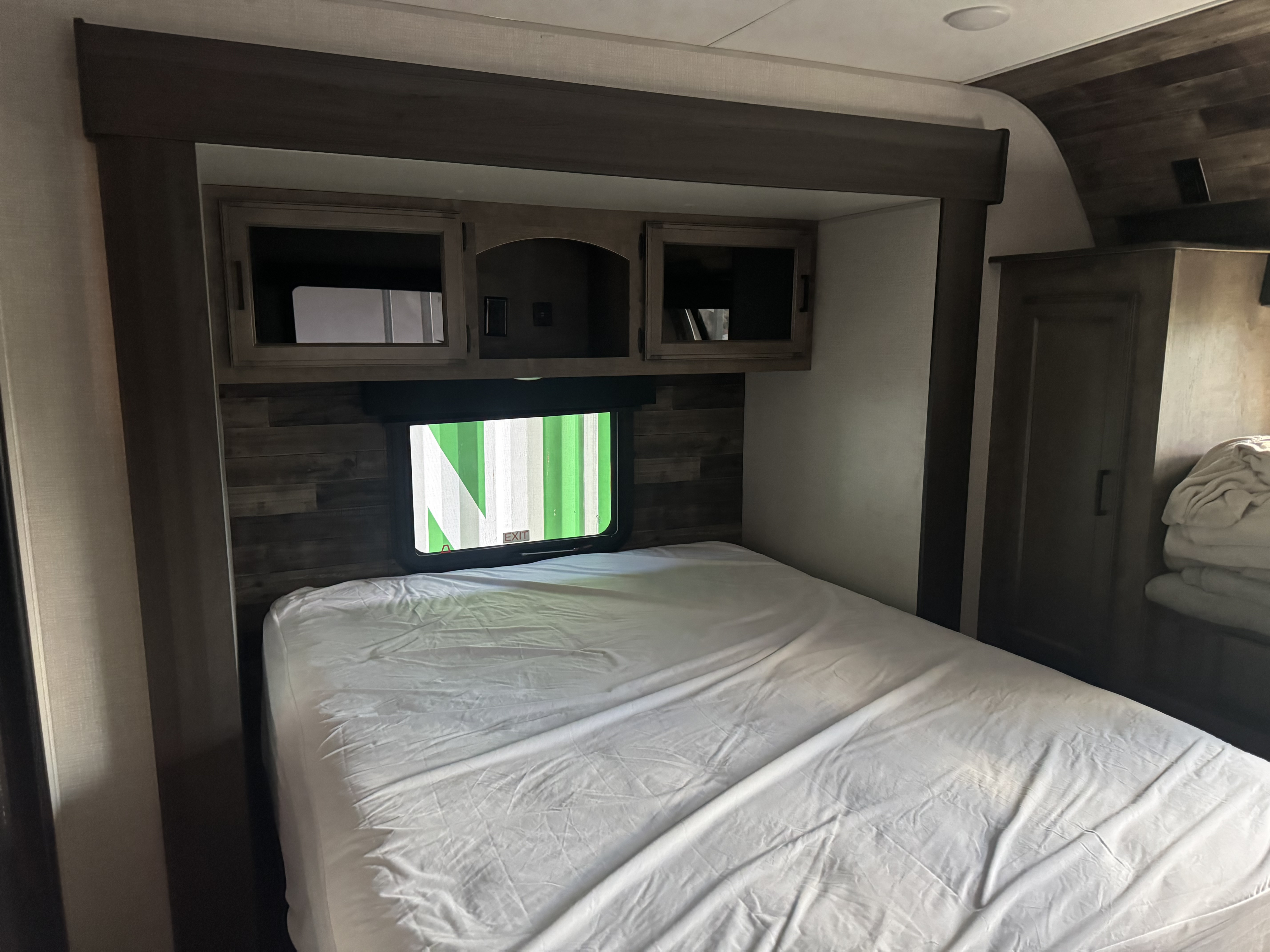 Cozy rv rental bedroom with a large bed, overhead cabinets, and a window, ideal for comfortable travel accommodations.. Sport Trek Touring 2021