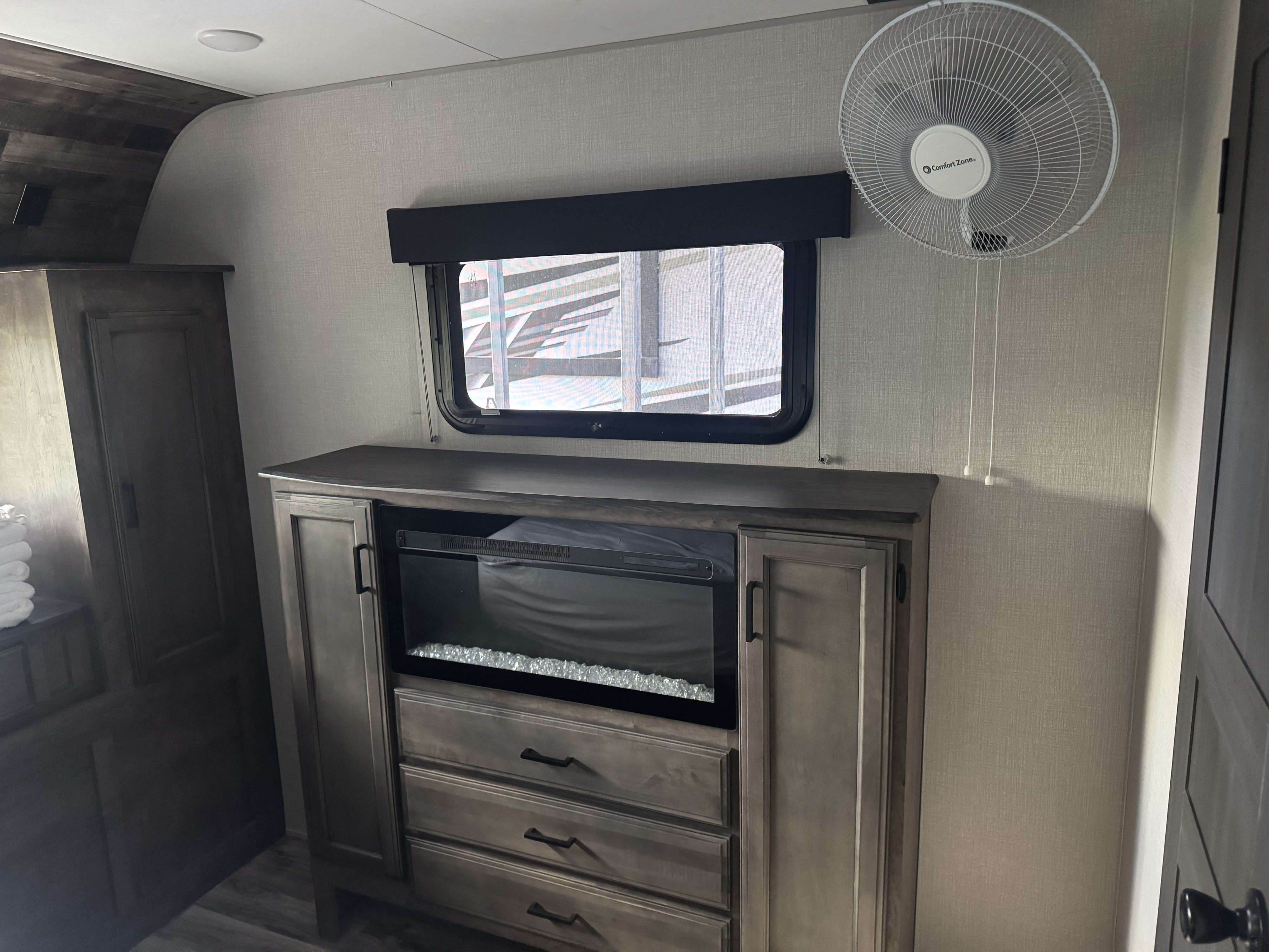 Cozy RV rental bedroom featuring a dresser with electric fireplace, window, and wall-mounted fan.. Sport Trek Touring 2021