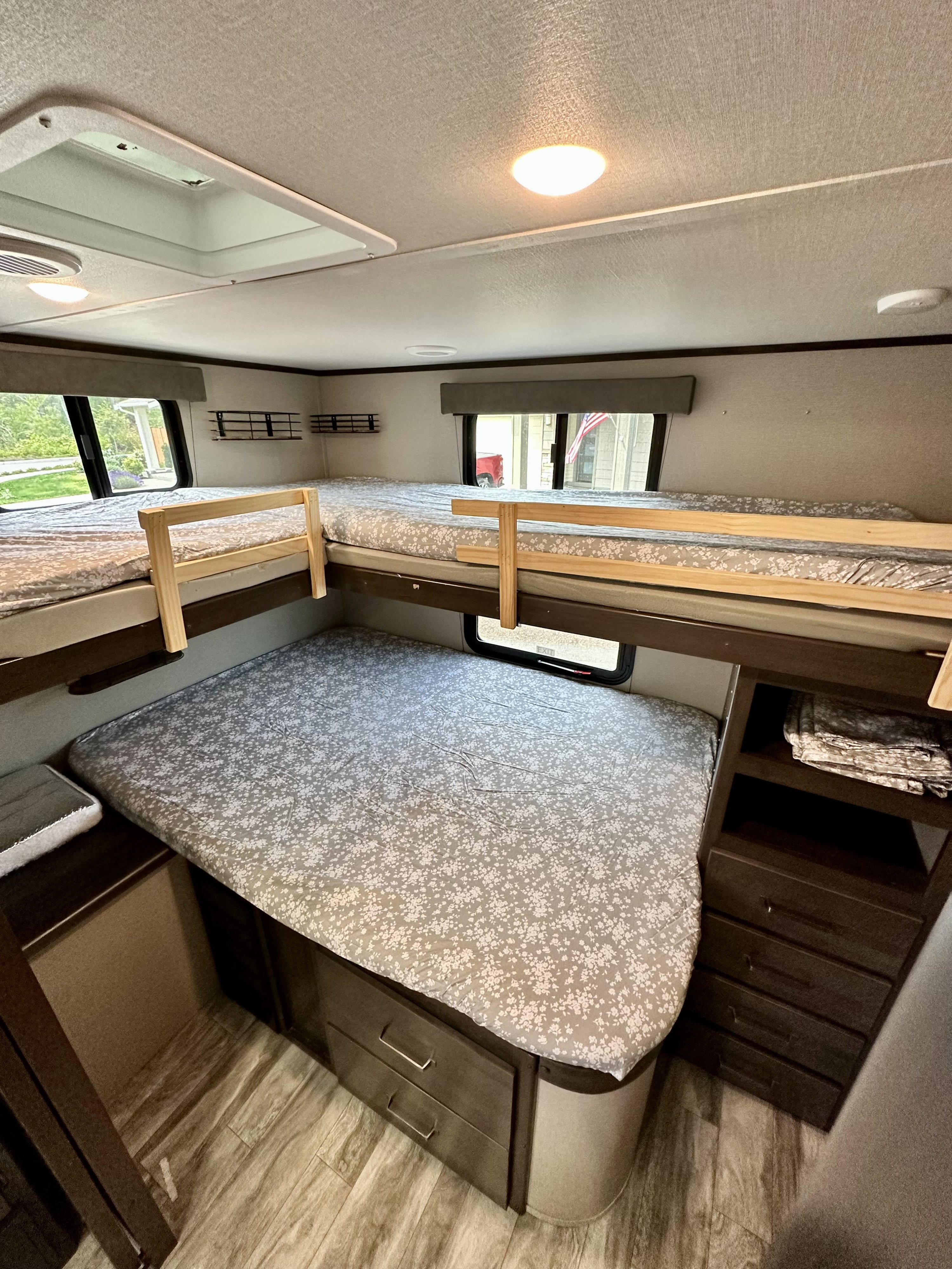 Inside an RV rental, this cozy bunkhouse features multiple beds with floral sheets, windows, built-in storage, and a skylight.. Grand Design Transcend Xplor 2022
