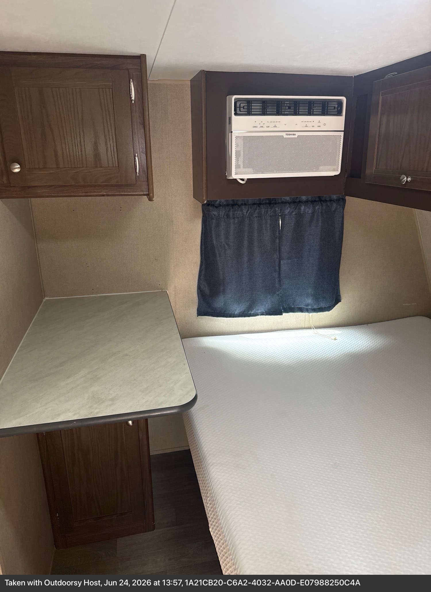 RV rental bedroom with a white mattress, small desk, dark wood overhead cabinets, and a wall-mounted Toshiba AC unit.. Keystone RV coleman lantern 17RD 2017