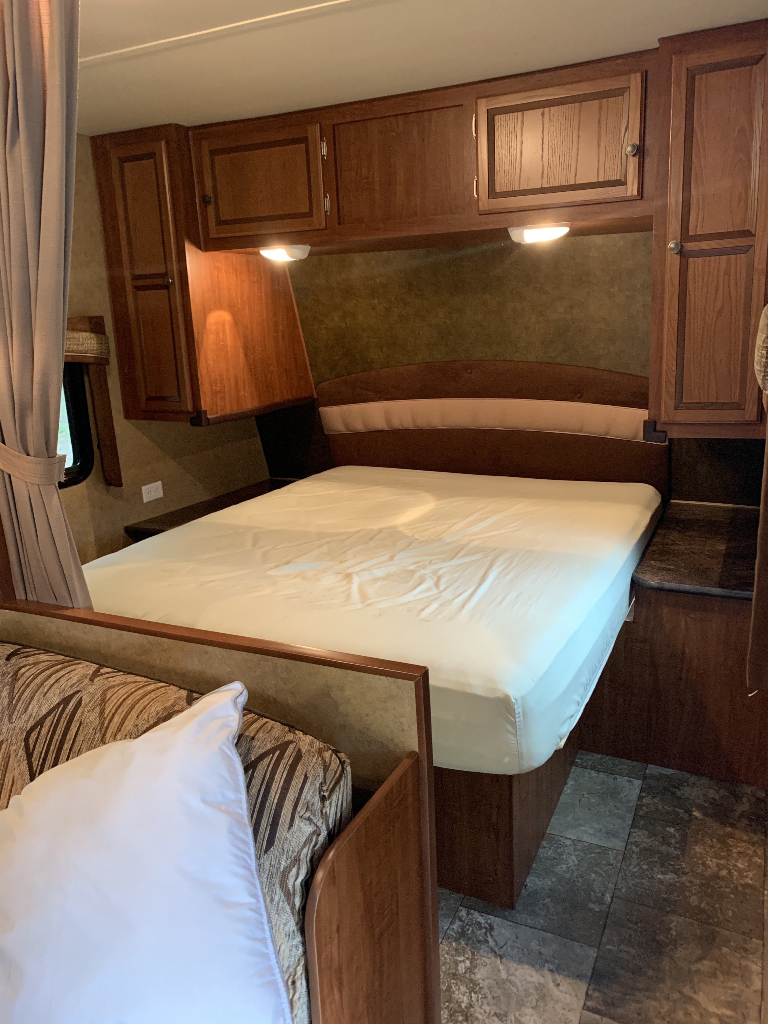 RV rental bedroom: A comfortable bed with white sheets, overhead wooden cabinets, window, and a sofa in the foreground.. Jayco Jay Flight 2013