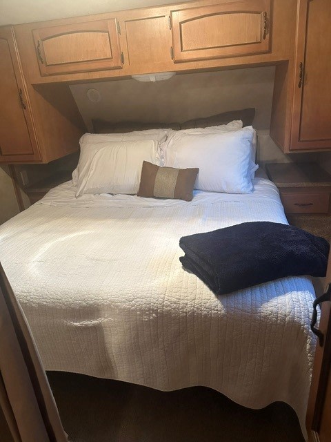 Comfortable RV rental bedroom featuring a bed with white linens, pillows, and practical overhead wood cabinets.. Forest River Puma 2011