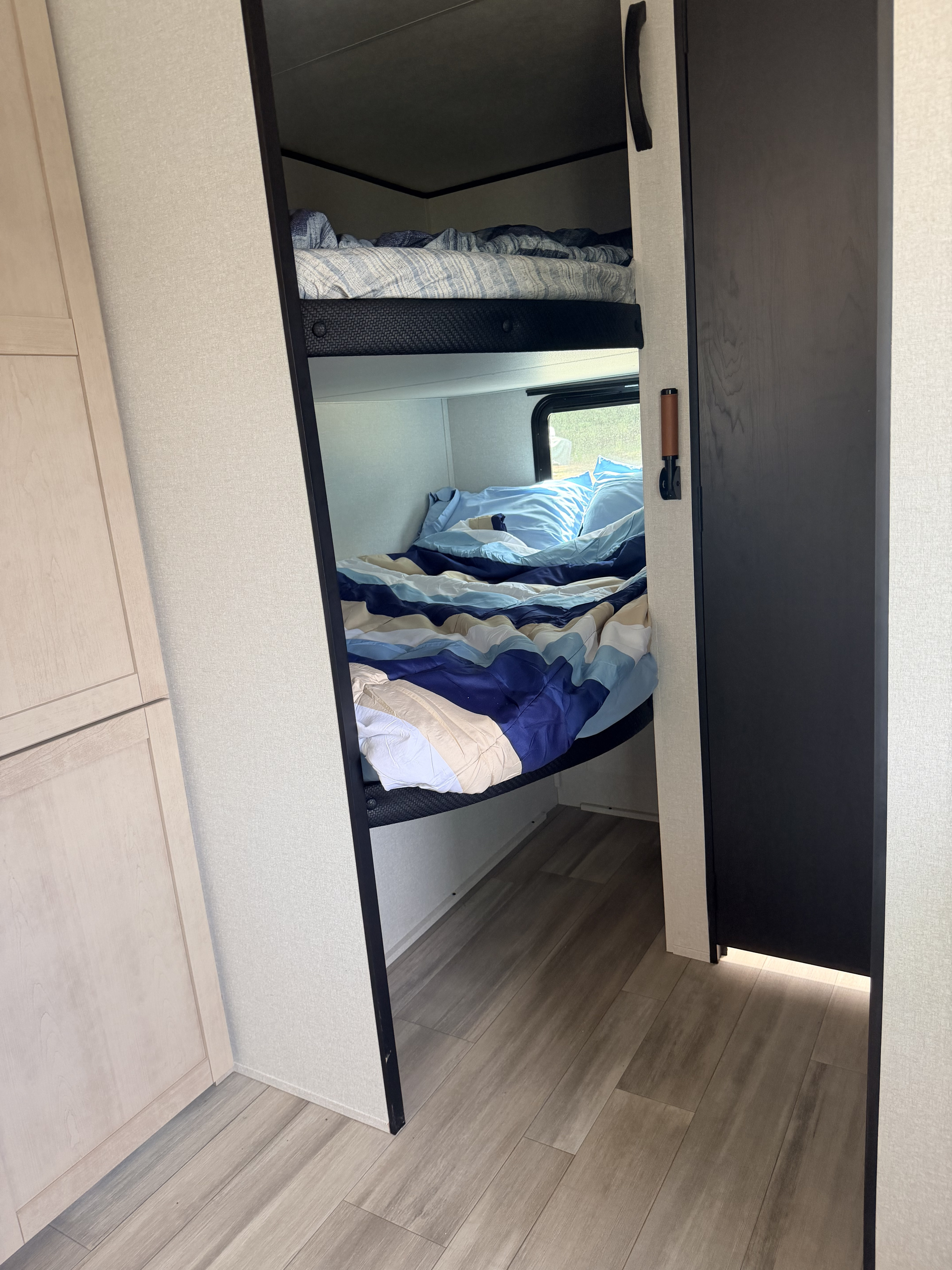 Inside an RV rental: two neatly made bunk beds with blue bedding, light wood cabinets, and a dark access door.. Wayfinder Go Play 26DBS 2026
