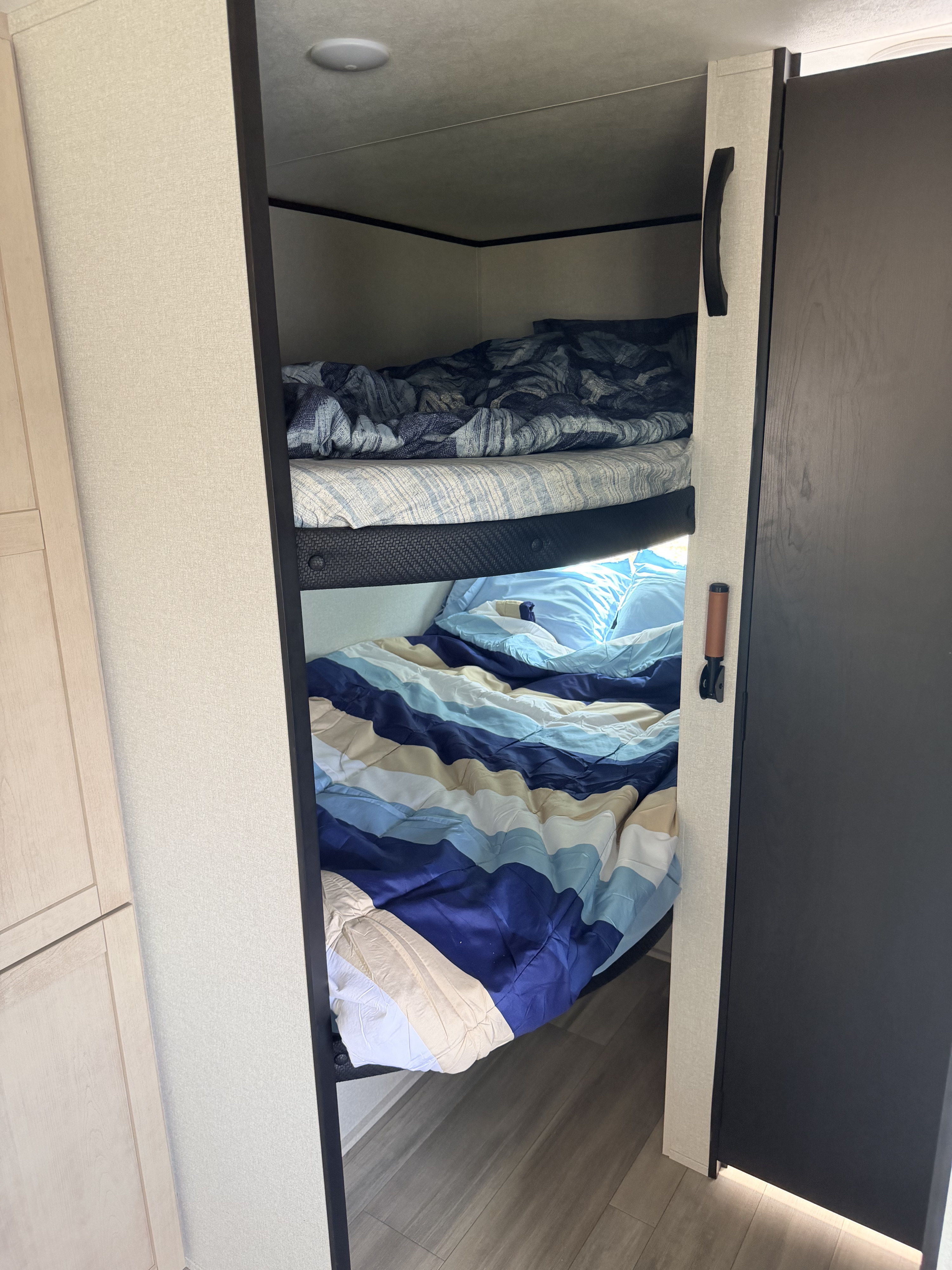 Cozy bunk beds with blue/white bedding inside a modern rv rental, featuring light interior walls & wood-look floor.. Wayfinder Go Play 26DBS 2026