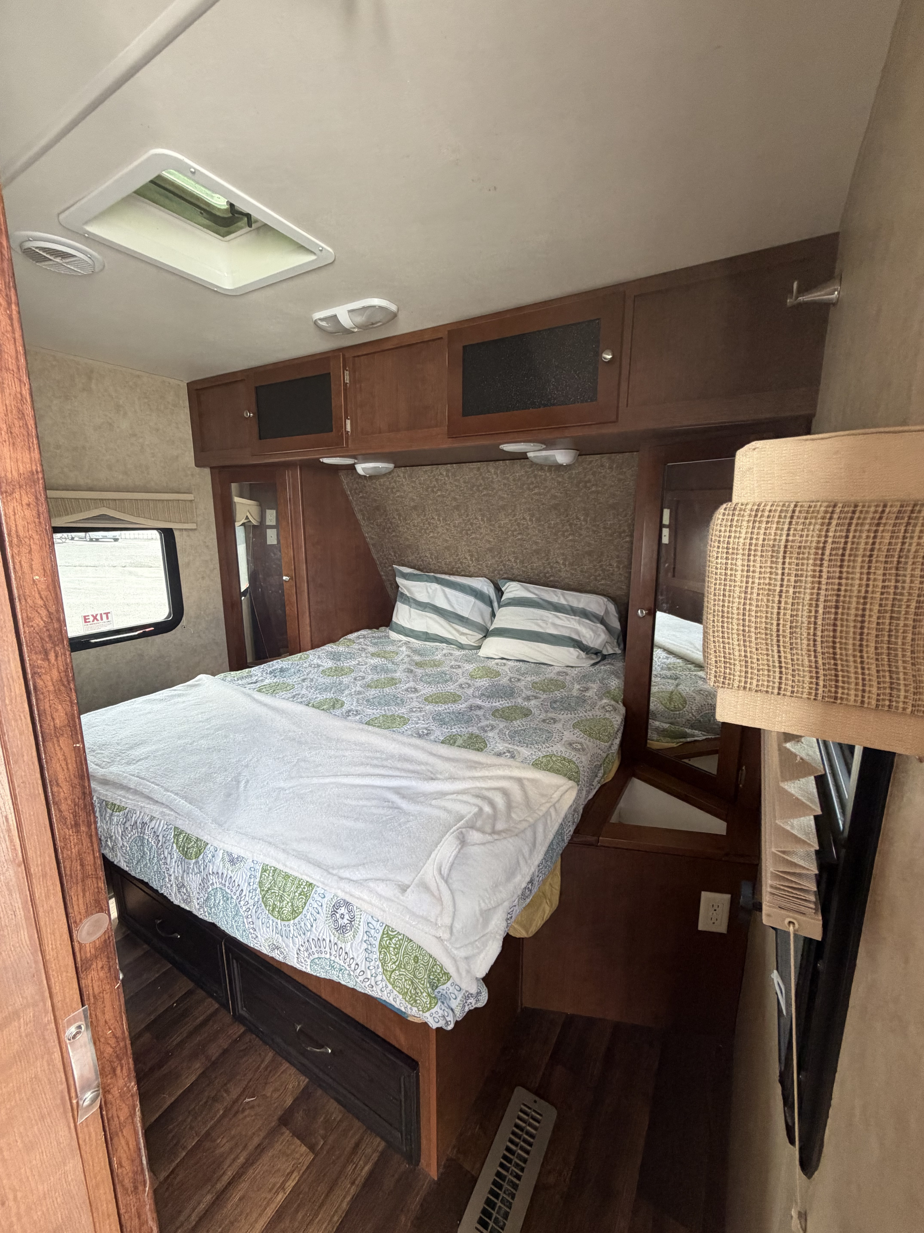Cozy RV rental bedroom featuring a comfy bed with patterned bedding, overhead storage, skylight, and window view.. Dutchmen Kodiak 2012