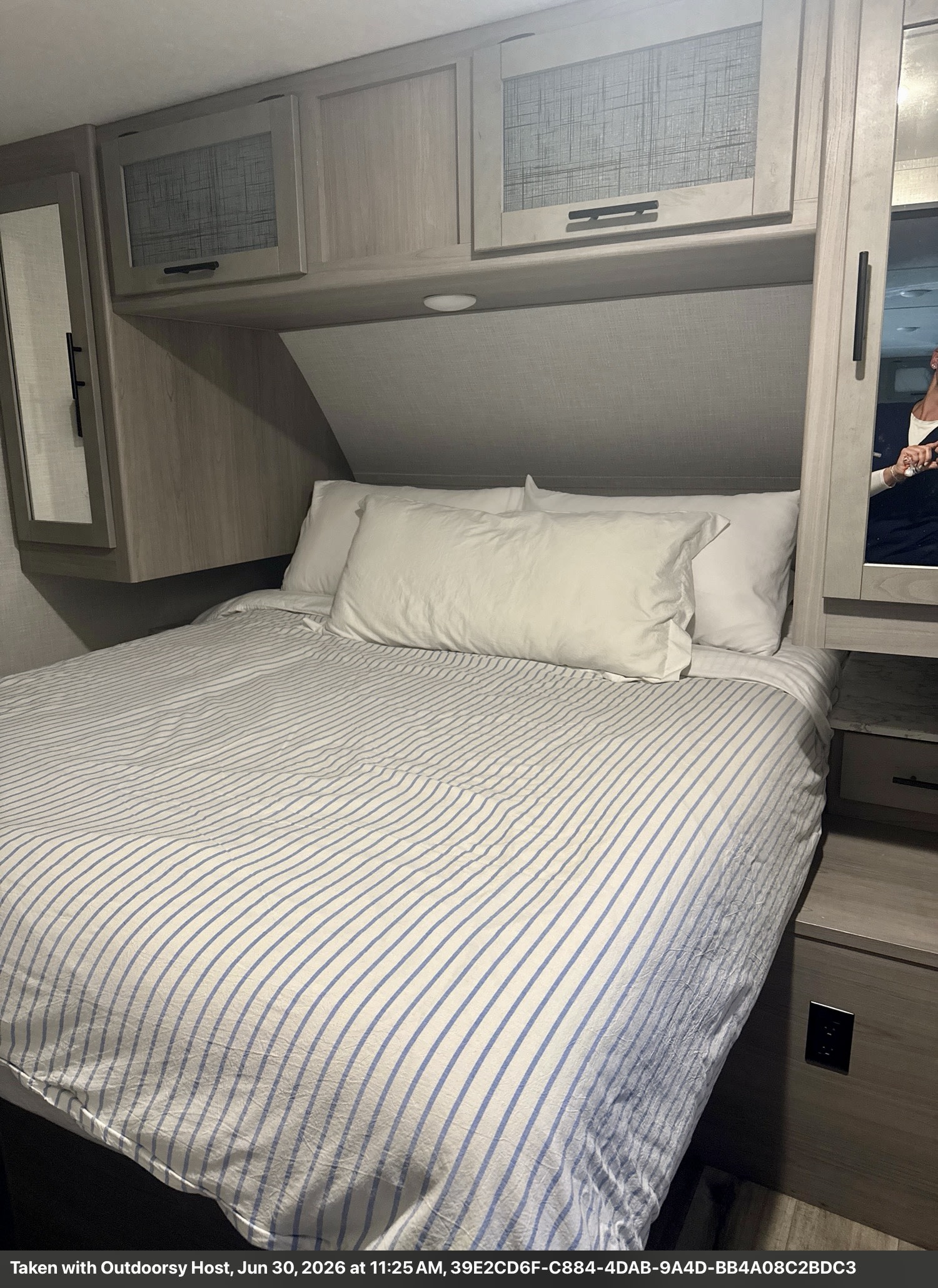 Experience comfort in this RV rental bedroom with striped bedding, soft pillows, and convenient overhead cabinets.. Keystone RV 2955RL 2022