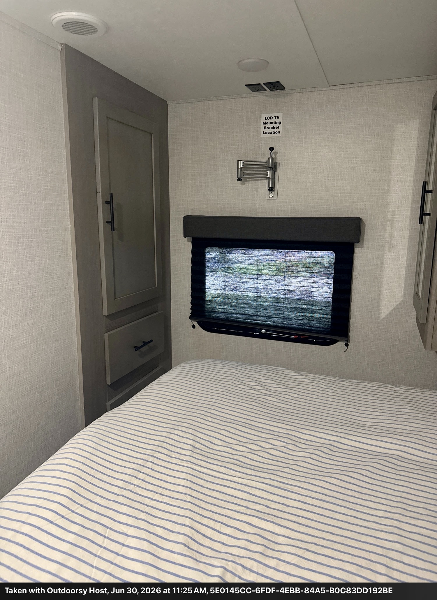 Cozy RV rental bedroom with a striped bed, built-in cabinet, window, and a wall-mounted TV bracket for convenience.. Keystone RV 2955RL 2022