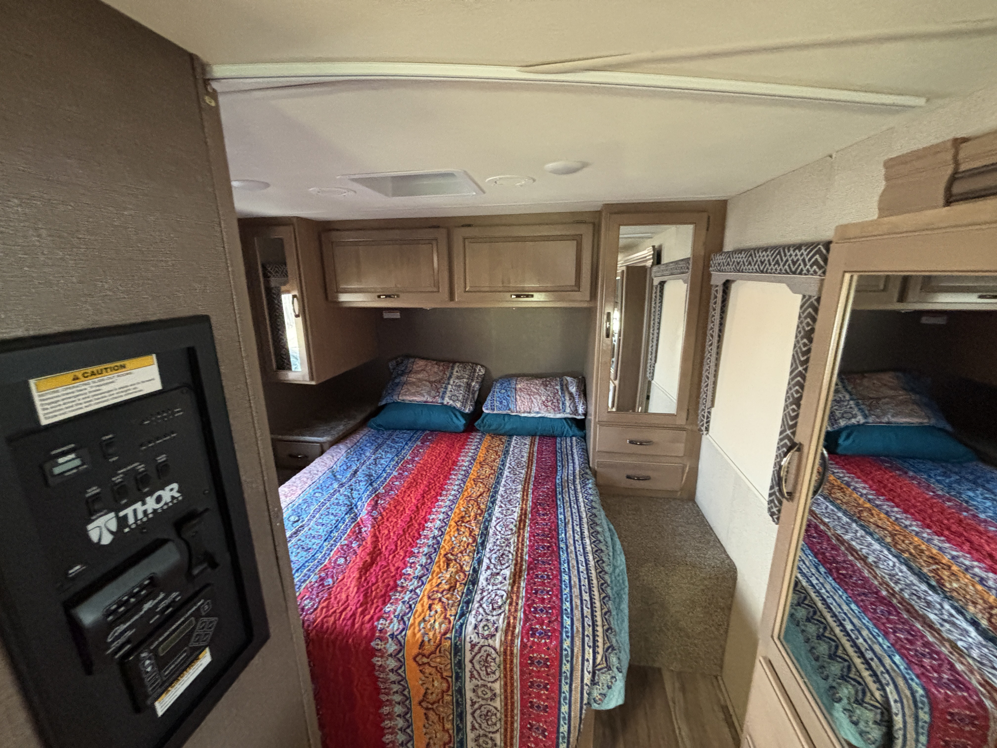 RV rental bedroom: Colorful, compact space with storage, a mirror, and a wall-mounted control panel.. Thor Four Winds 2018