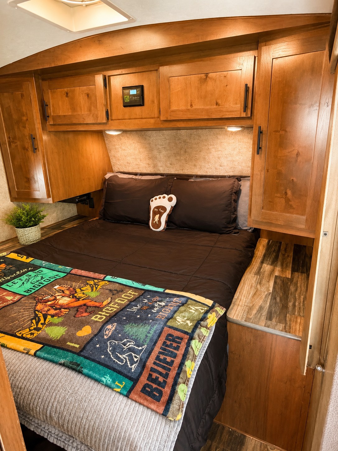 This RV rental bedroom offers a cozy Bigfoot-themed escape with warm wood cabinetry and a comfy "Believer" blanket.. Outdoors RV Mountain Trax Backcountry 2024