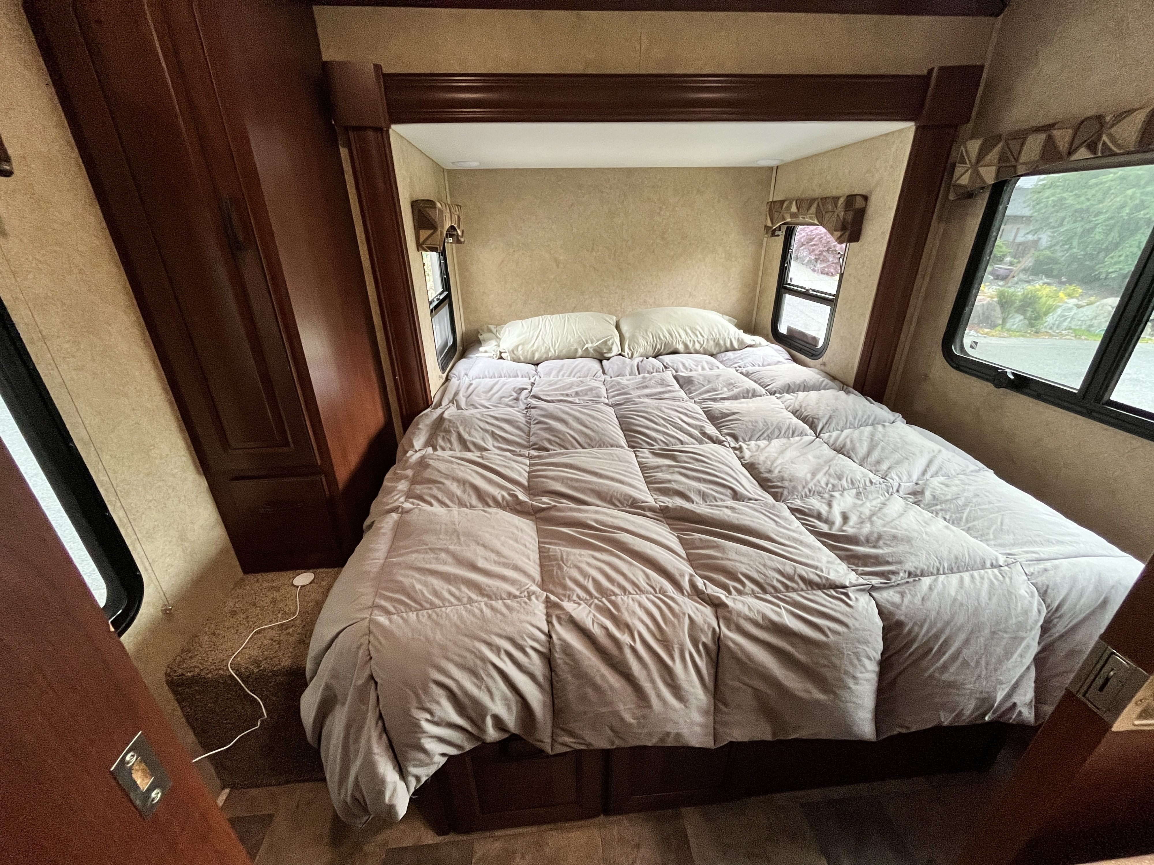 Comfortable rv rental bedroom with a grey comforter, pillows, windows, and rich wood cabinetry. Ideal for travel.. Forest River Solera 2013