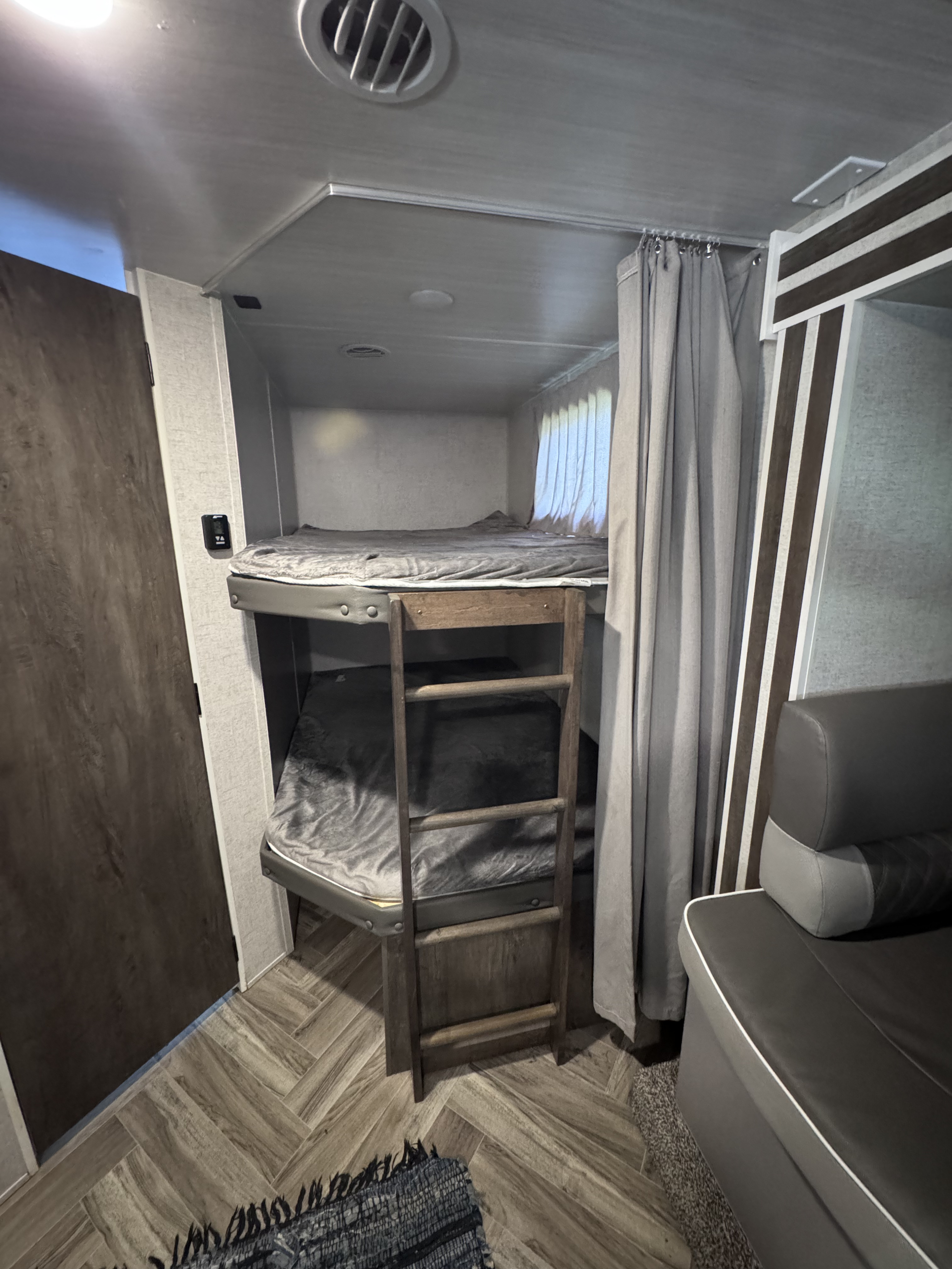 Interior of an RV rental with modern bunk beds, a ladder, gray bedding, and a sofa, creating a compact sleeping and living area.. Forest River Salem Cruise Lite 2022