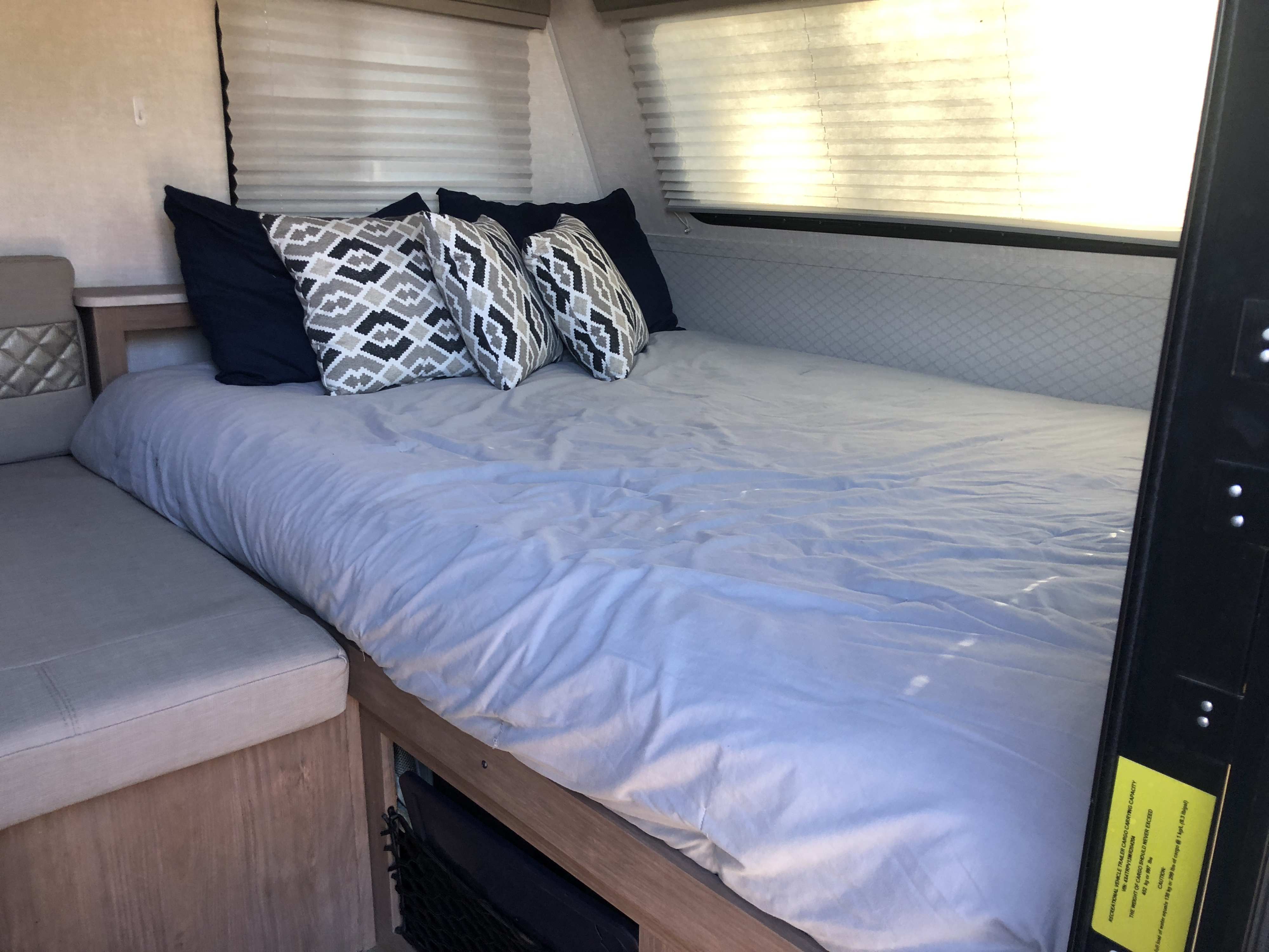 Cozy RV rental bedroom with a comfortable bed, stylish pillows, window blinds, and a visible cargo capacity sticker.. Forest River No Boundaries 19.7 2021