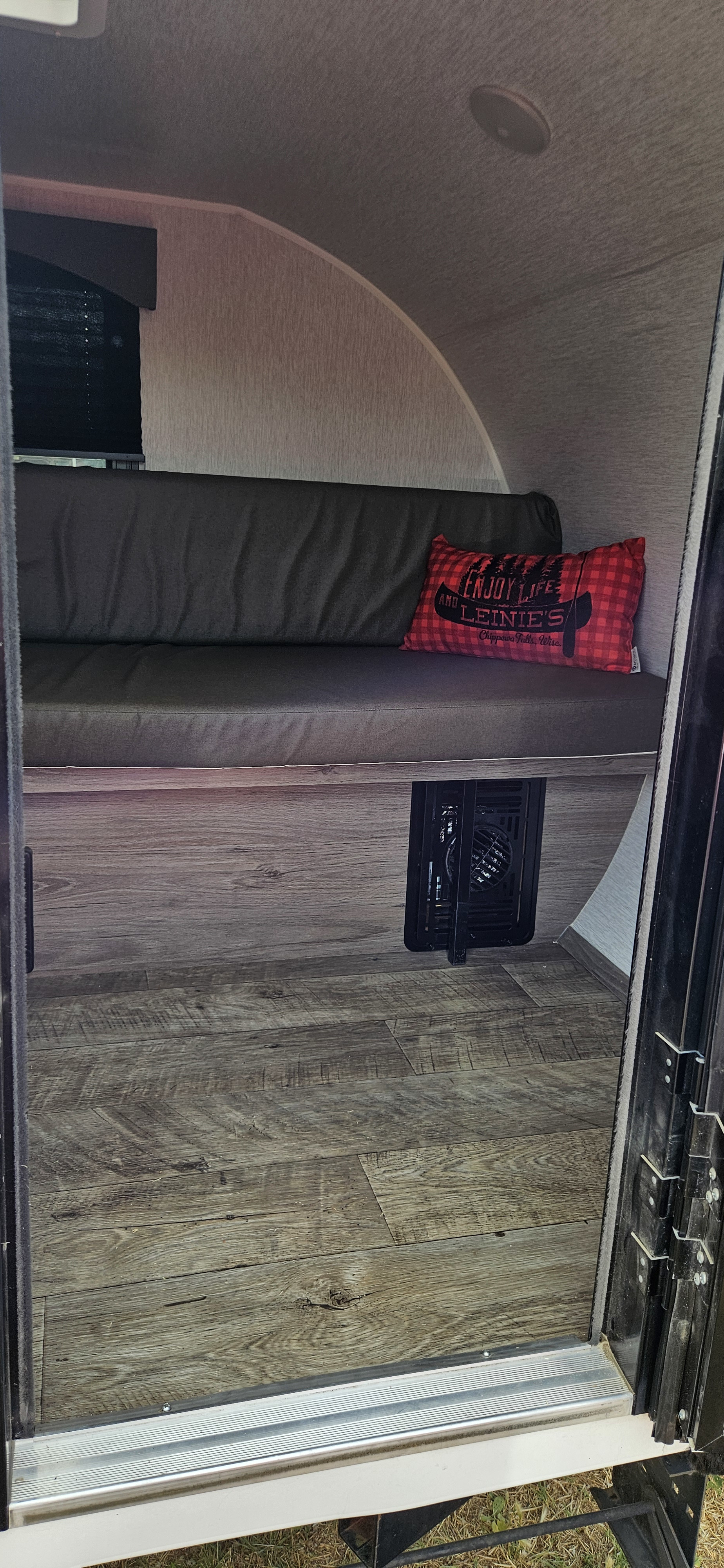 Inside this RV rental: A cozy bench seat with a red plaid pillow, wood floor, and a heater vent in the compact camper.. Sunset Park RV SunRay 2024