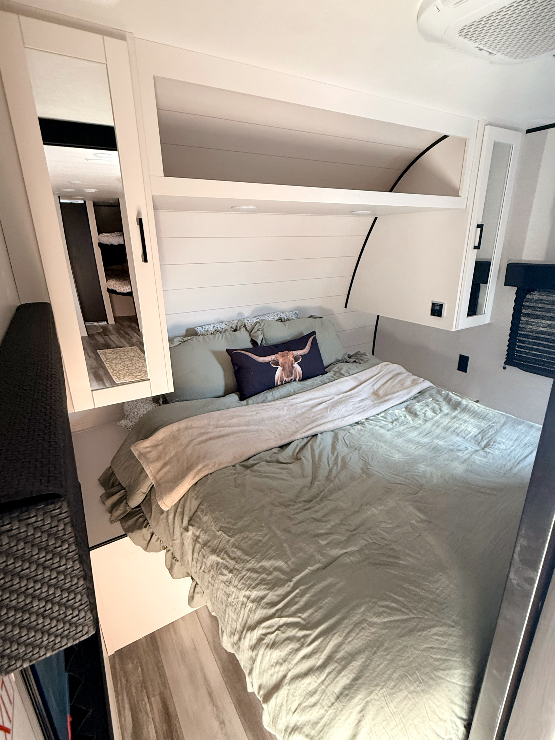 Cozy RV rental bedroom features a green bed with a longhorn pillow, overhead cabinets, and a mirror reflecting bunk beds.. Jayco Flight SLX 261BHS 2026