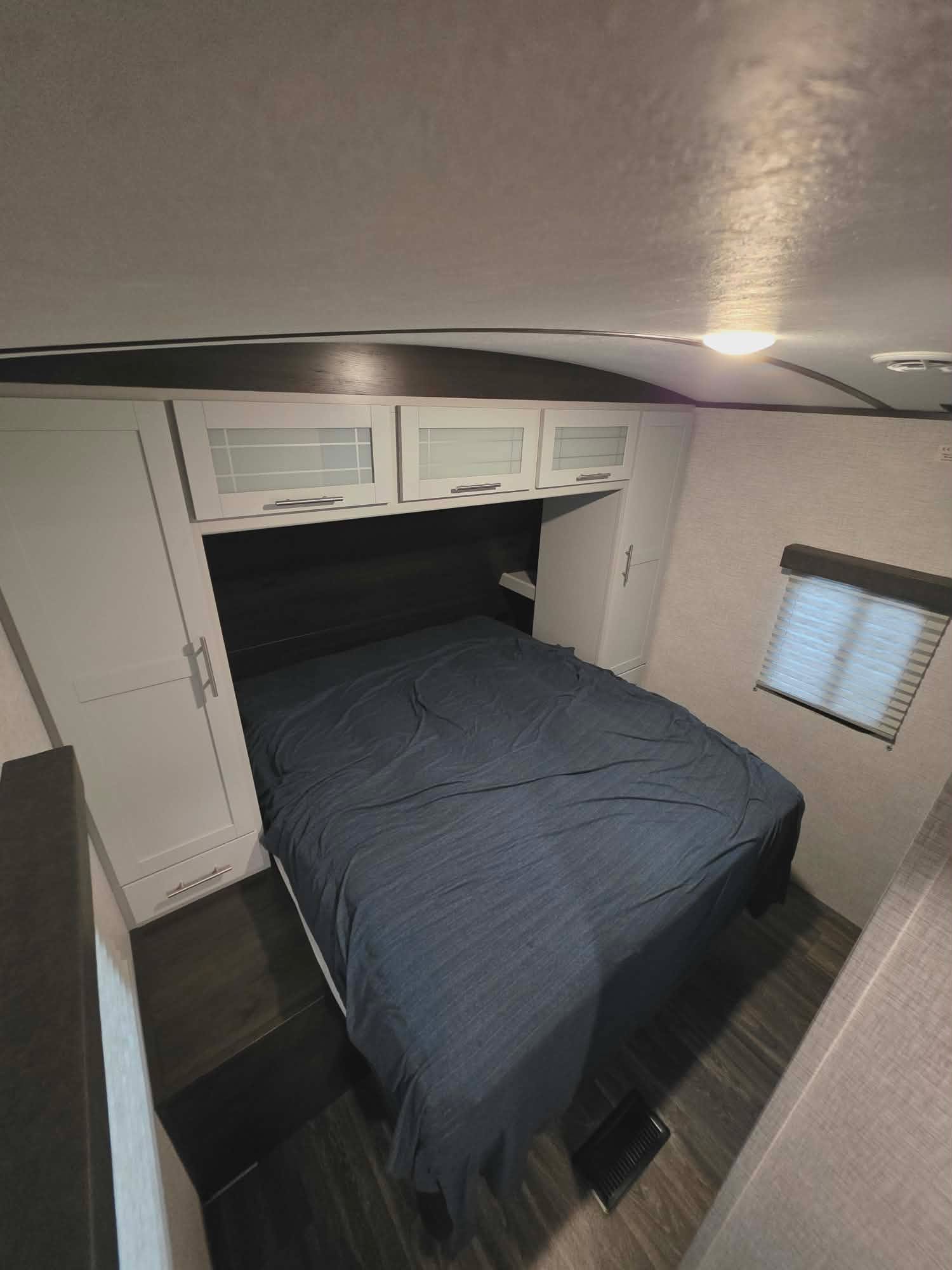Cozy rv rental bedroom featuring a bed with dark blue sheets, white cabinets, and a window with blinds for comfortable stays.. Keystone RV Bullet Ultra Lite 2021