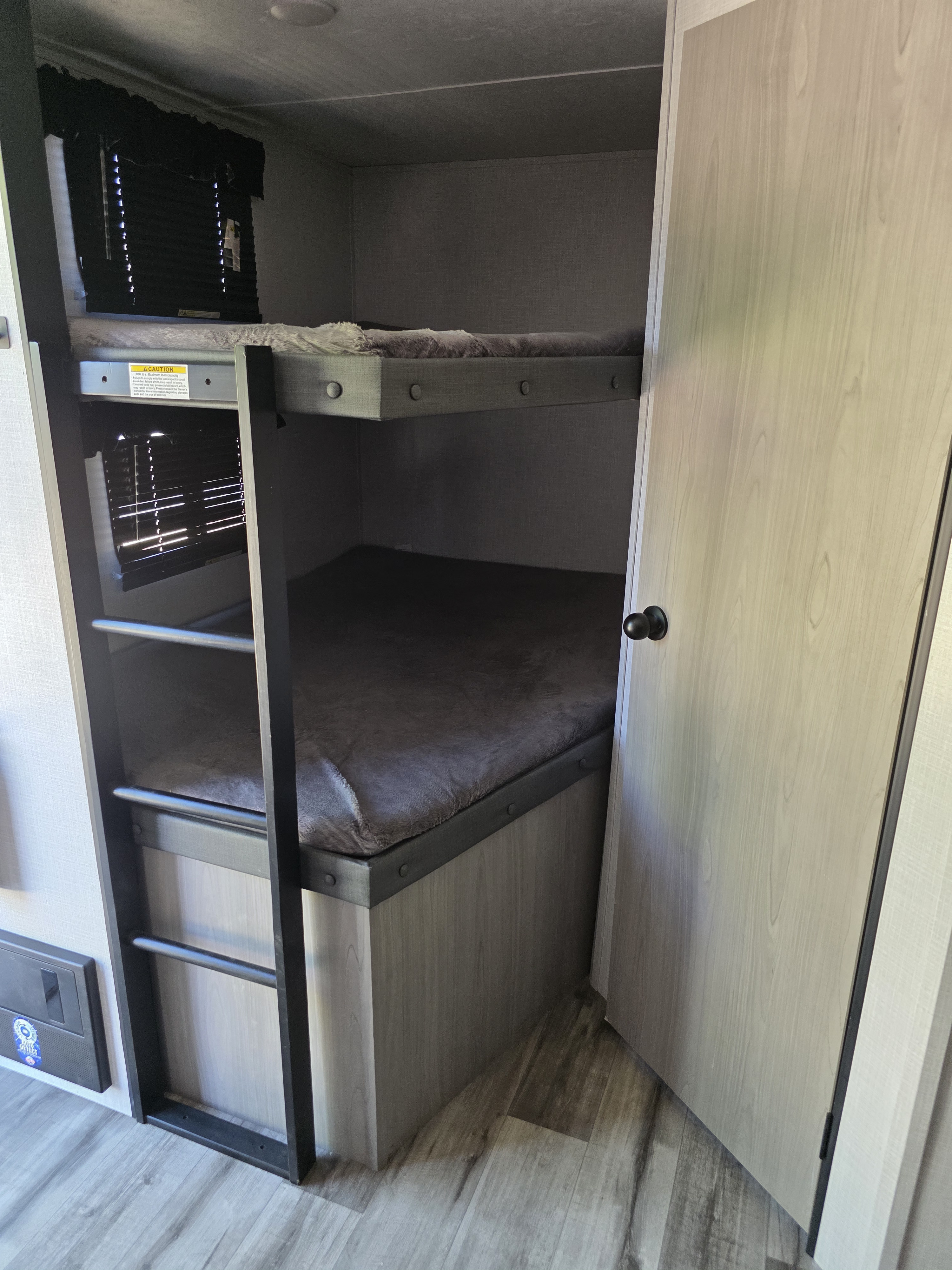 Inside an rv rental, featuring a set of modern bunk beds with a ladder, blinds, and a neutral color scheme.. Dutchmen Coleman Light 2023