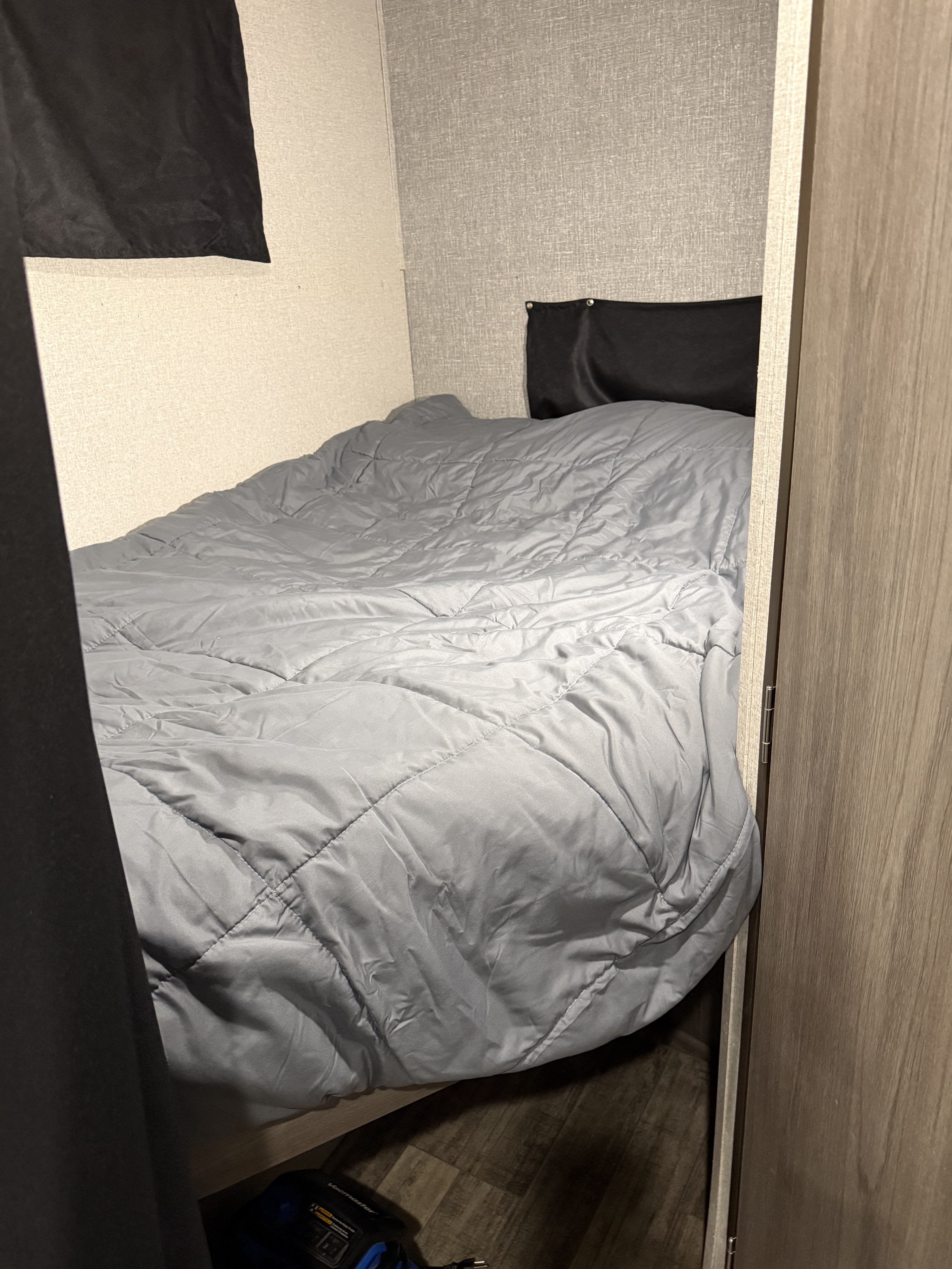 Cozy gray bed and comforter in an RV rental sleeping nook, with textured walls and a partial view of a vacuum.. Keystone RV 270BH 2022