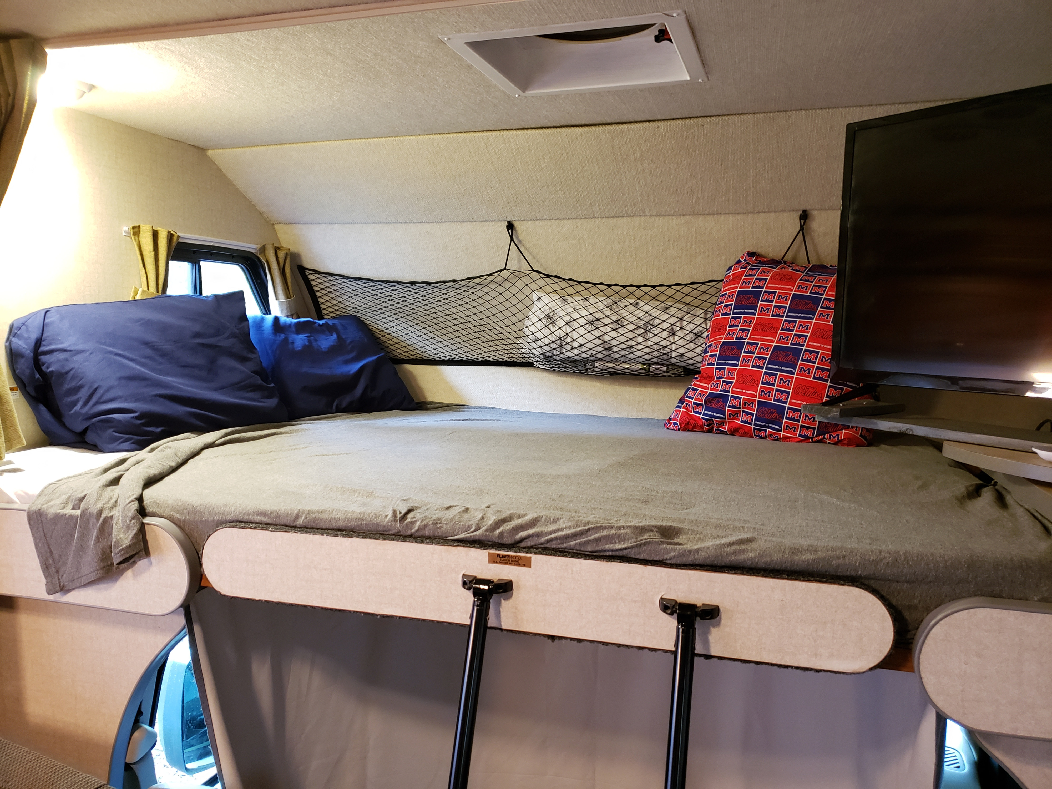 RV rental interior featuring a comfortable cab-over bunk bed, overhead storage net, and TV, perfect for travel.. Fleetwood Tioga 31M 2007