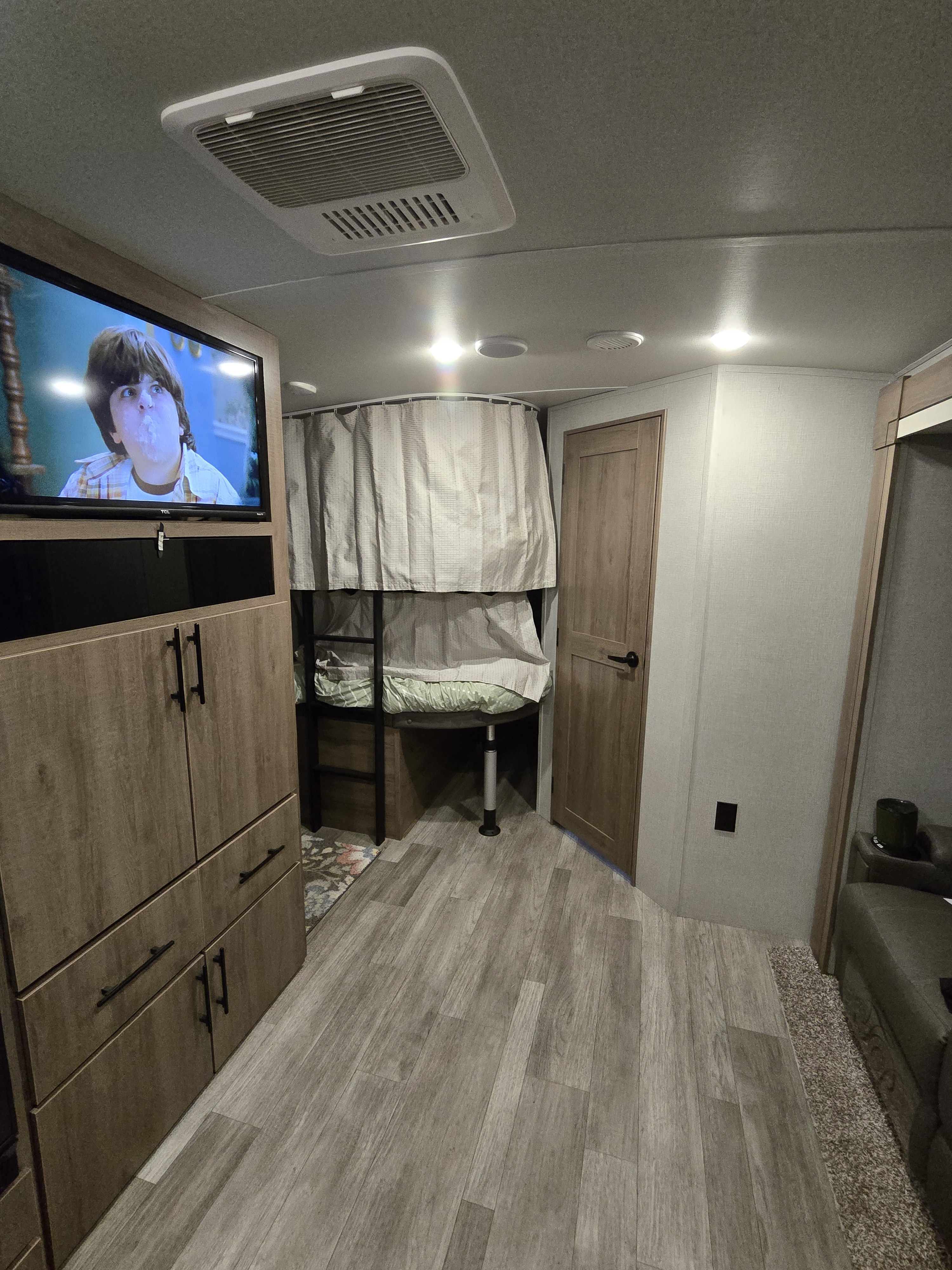Cozy rv rental interior featuring a TV, bunk beds with privacy curtains, a door, and wood-look flooring.. Grand Design Imagine 2023