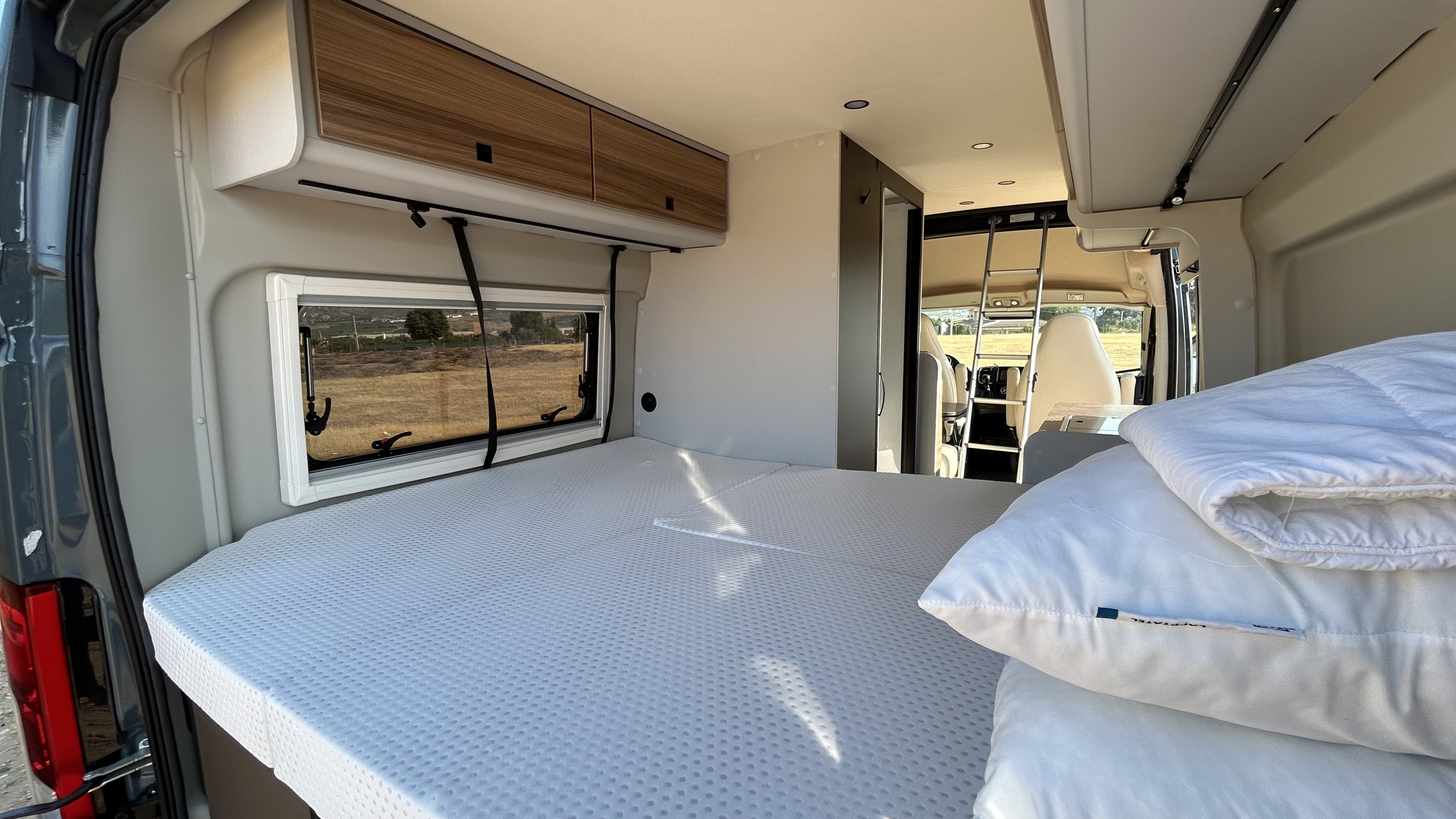 Cozy rv rental interior with a comfortable bed, overhead storage, and a view, perfect for road trips.. BURSTNER B66 2024