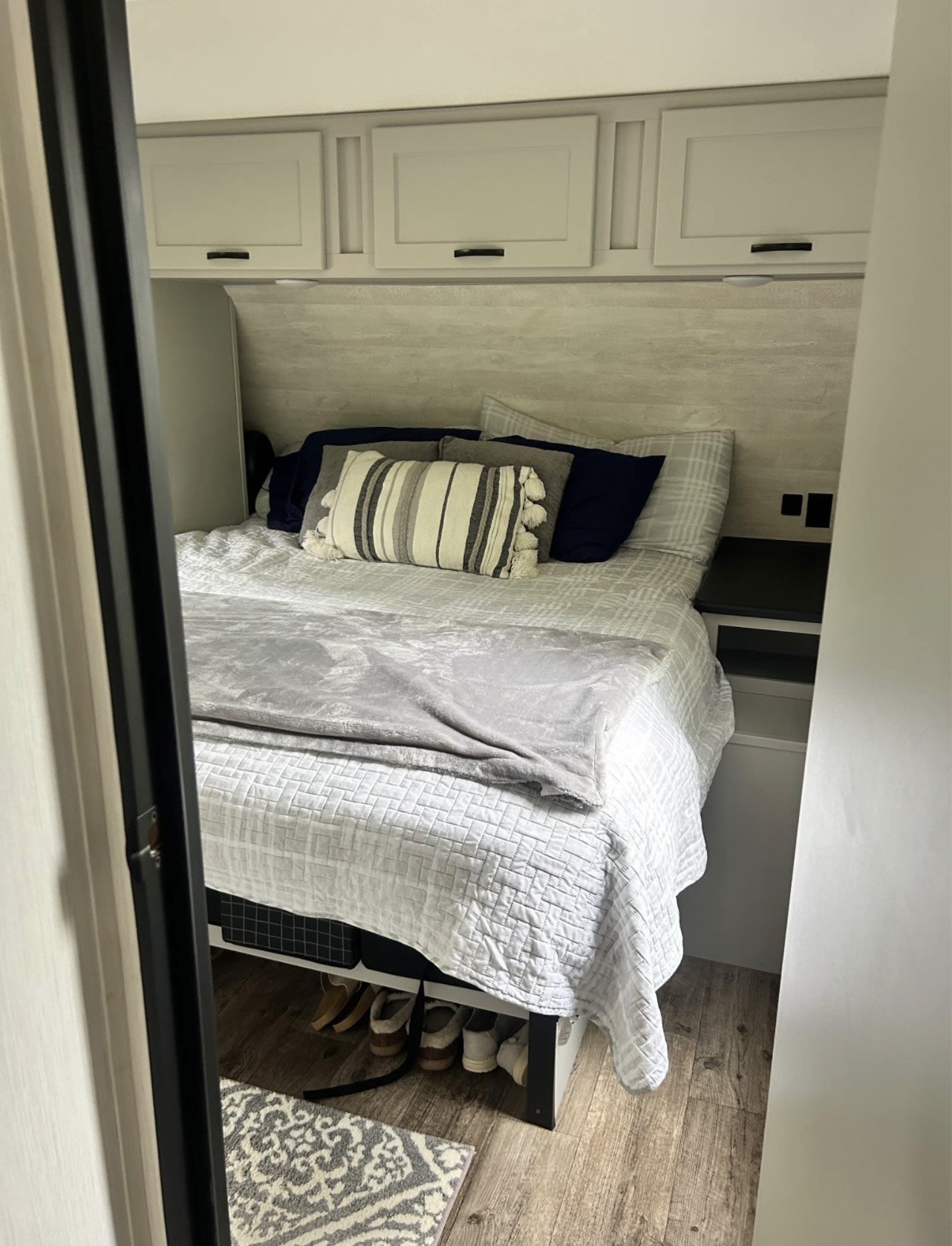 Inside a cozy RV rental: a comfortable bed with pillows, overhead cabinets, and practical under-bed storage.. Forest River Vibe 2021