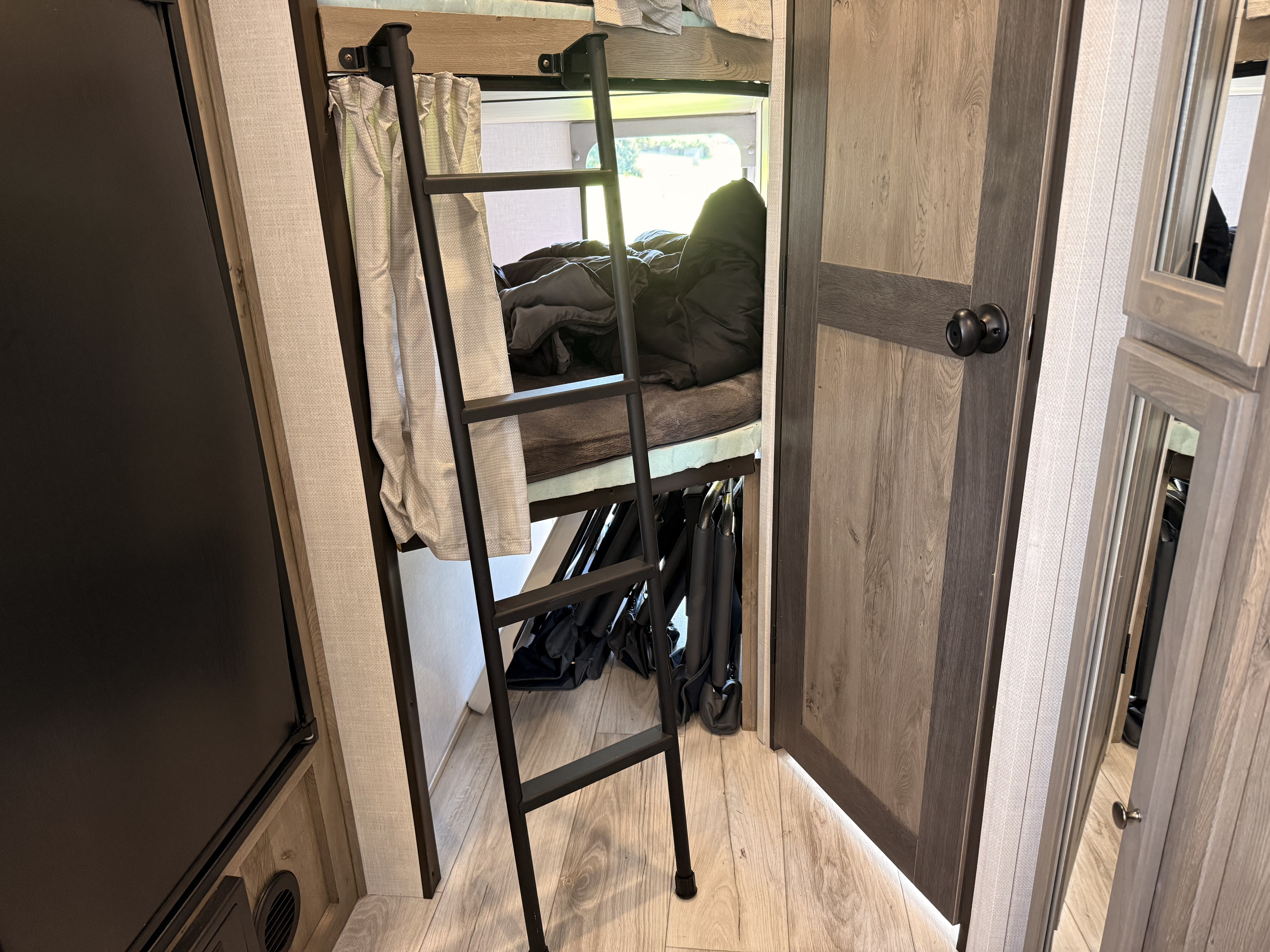 RV rental: Bunk beds with a black ladder, dark bedding, and light wood cabinetry. Provides extra sleeping in a cozy space.. Forest River Surveyor Legend 2022