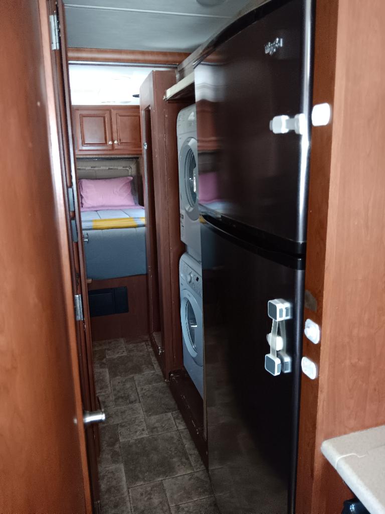 Tour this RV rental's interior: black fridge, stacked washer/dryer, and a cozy bedroom are visible down the hallway.. Thor Palazzo 2014