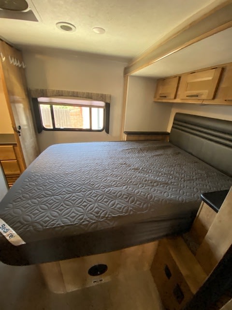 RV rental bedroom: comfortable space with a large bed, dark headboard, window, and overhead cabinets for storage.. Coachmen Leprechaun 311fs 2020