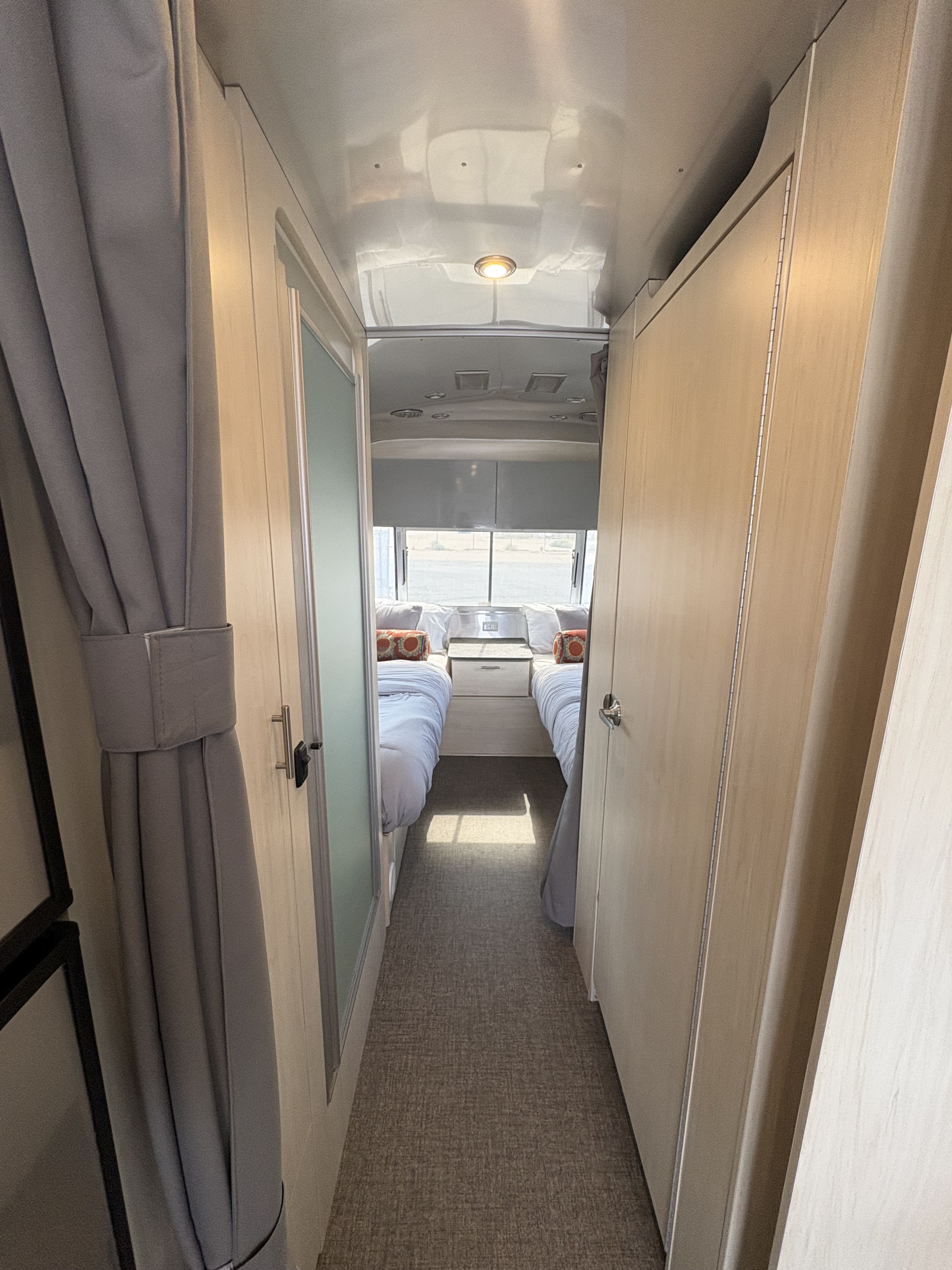 View down an RV rental hallway towards a bedroom with two neatly made twin beds, light wood cabinetry, and carpet flooring.. Airstream Flying Cloud 2021