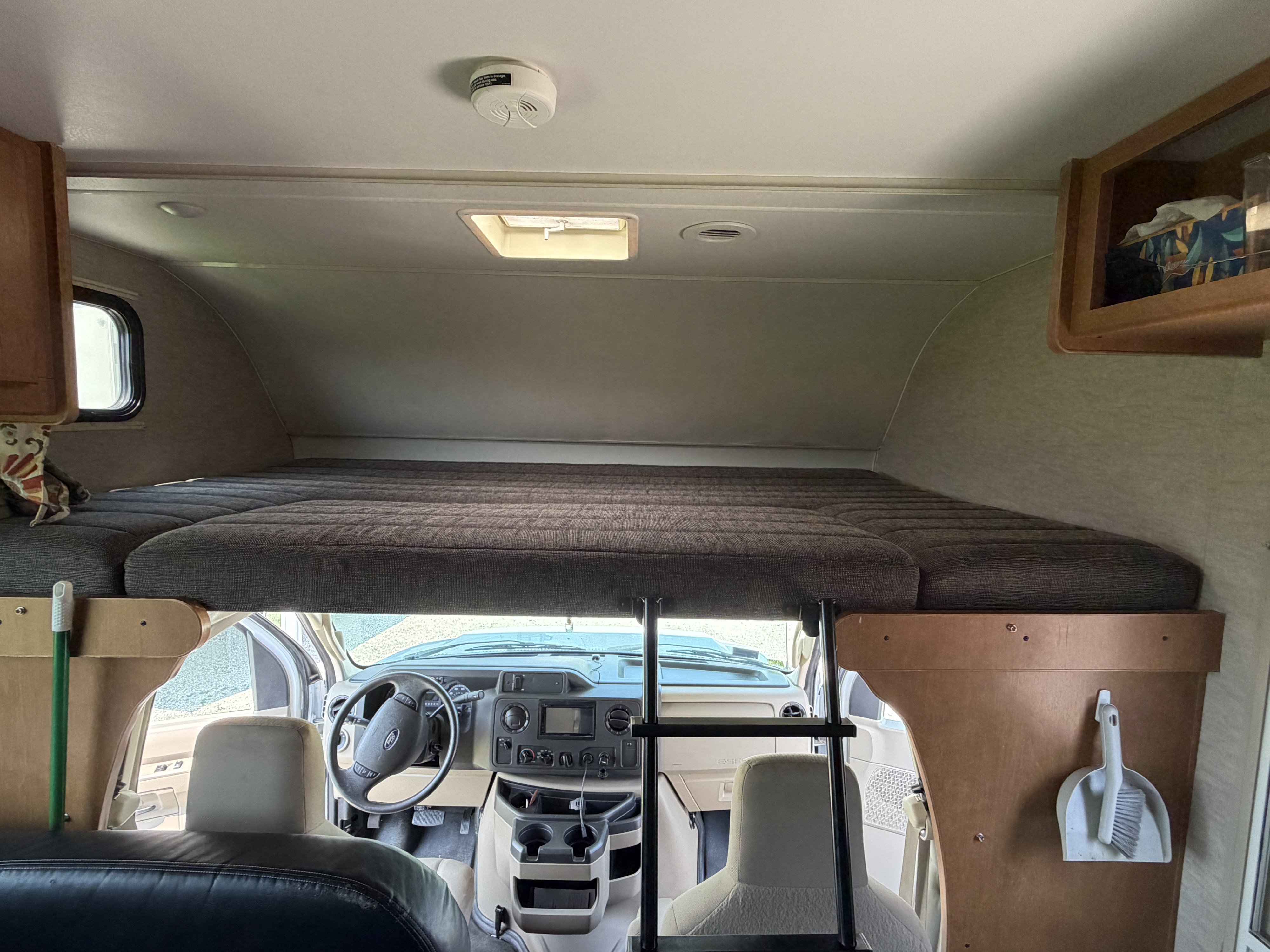 RV rental interior shows the overhead bed above the cockpit area. A smoke detector is on the ceiling; a ladder provides bunk access.. Itasca Spirit 2016