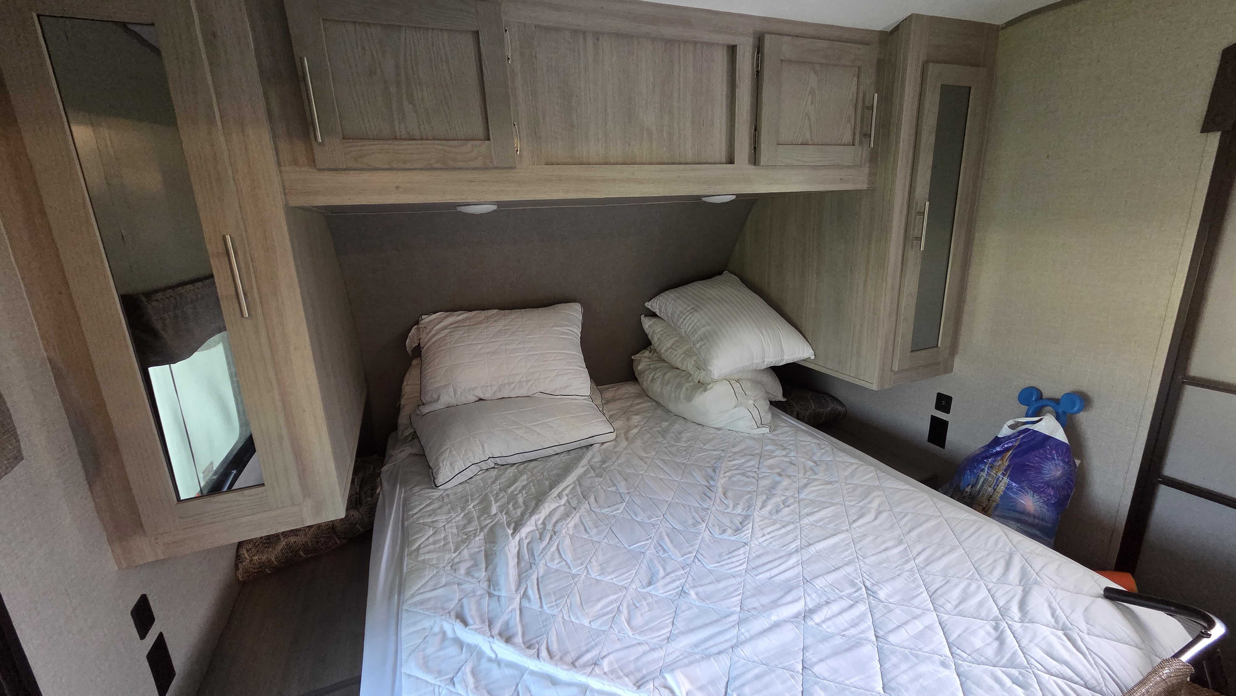 RV rental bedroom: comfortable bed with white bedding, overhead storage cabinets, and a mirrored wardrobe for a functional travel stay.. Forest River Coachmen Catalina Legacy 2022