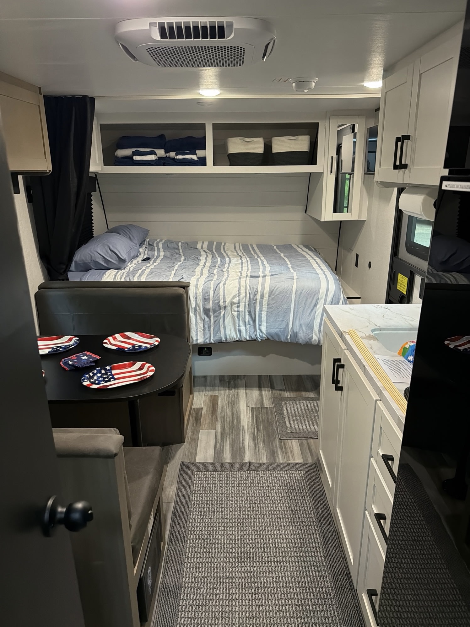 Cozy RV rental interior with a comfy bed, dining area with patriotic plates, and compact kitchen. Perfect for travel.. Jayco Jay Flight SLX 2026