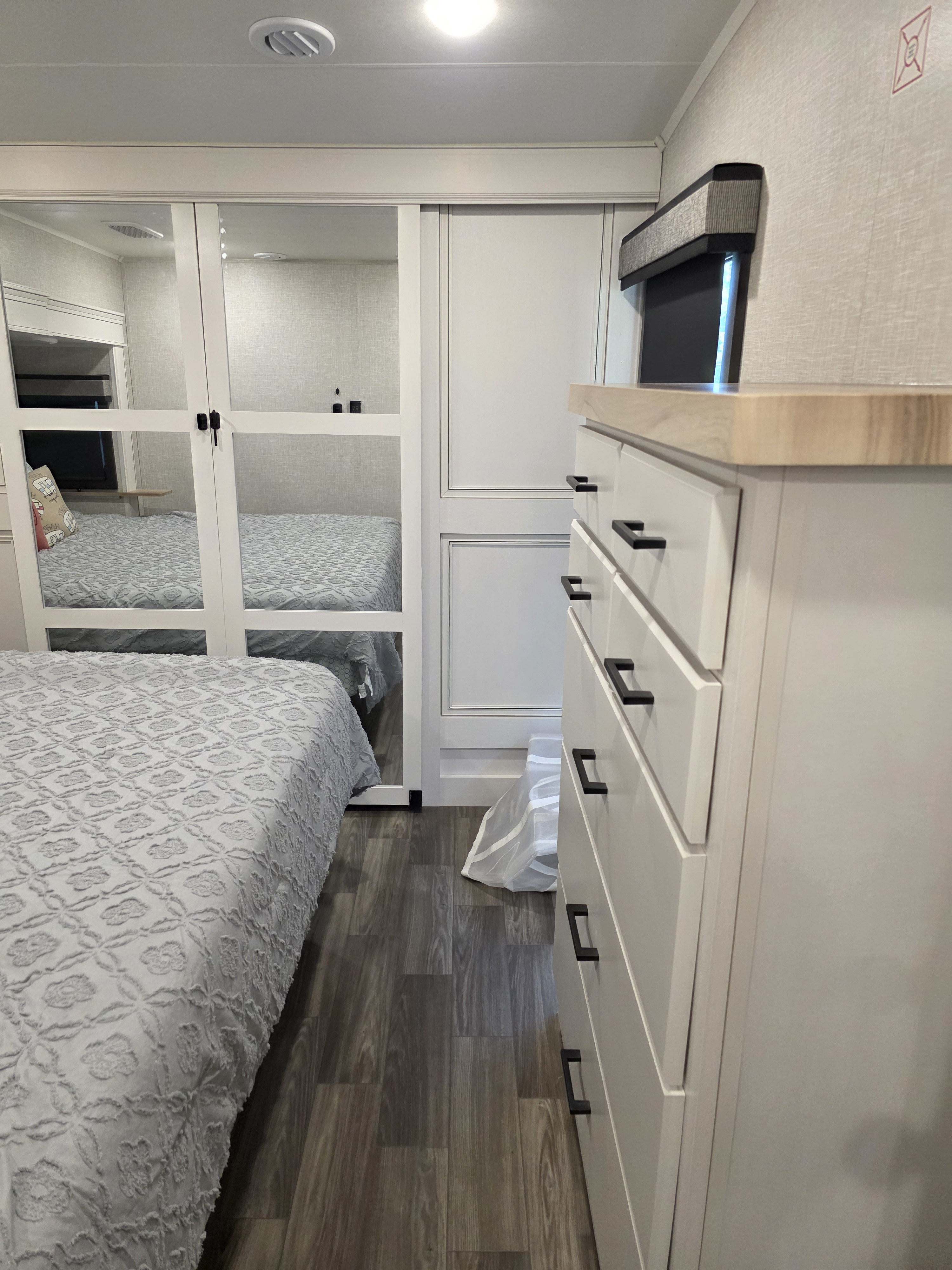 RV rental bedroom showcasing a patterned bed, mirrored closet, white dresser with black pulls, and wood flooring.. Jayco Eagle 2024