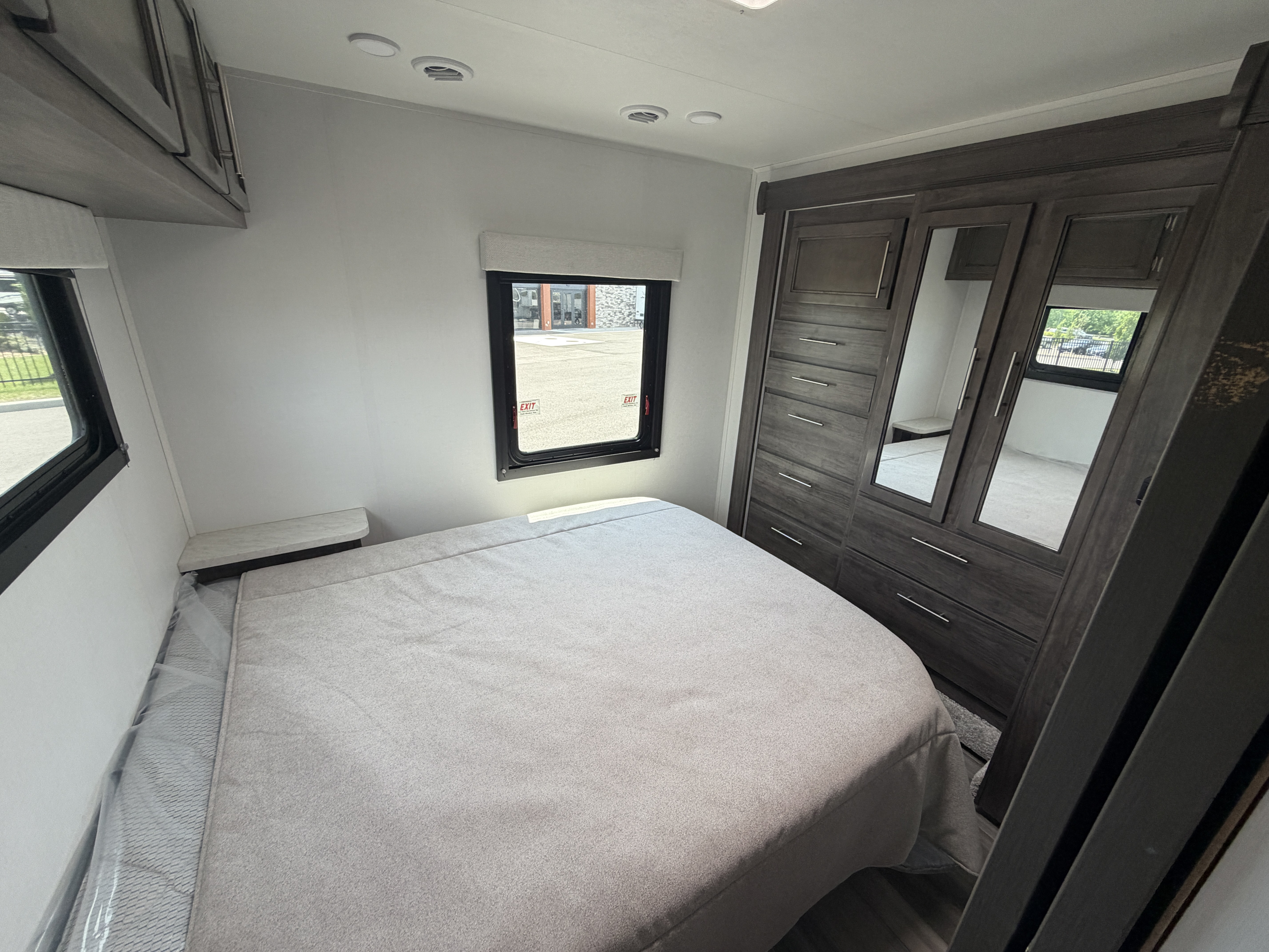 RV rental bedroom with a light grey bed, built-in mirrored wardrobe, and two windows. A modern and functional interior.. Jayco Redhawk SE 31FF 2026
