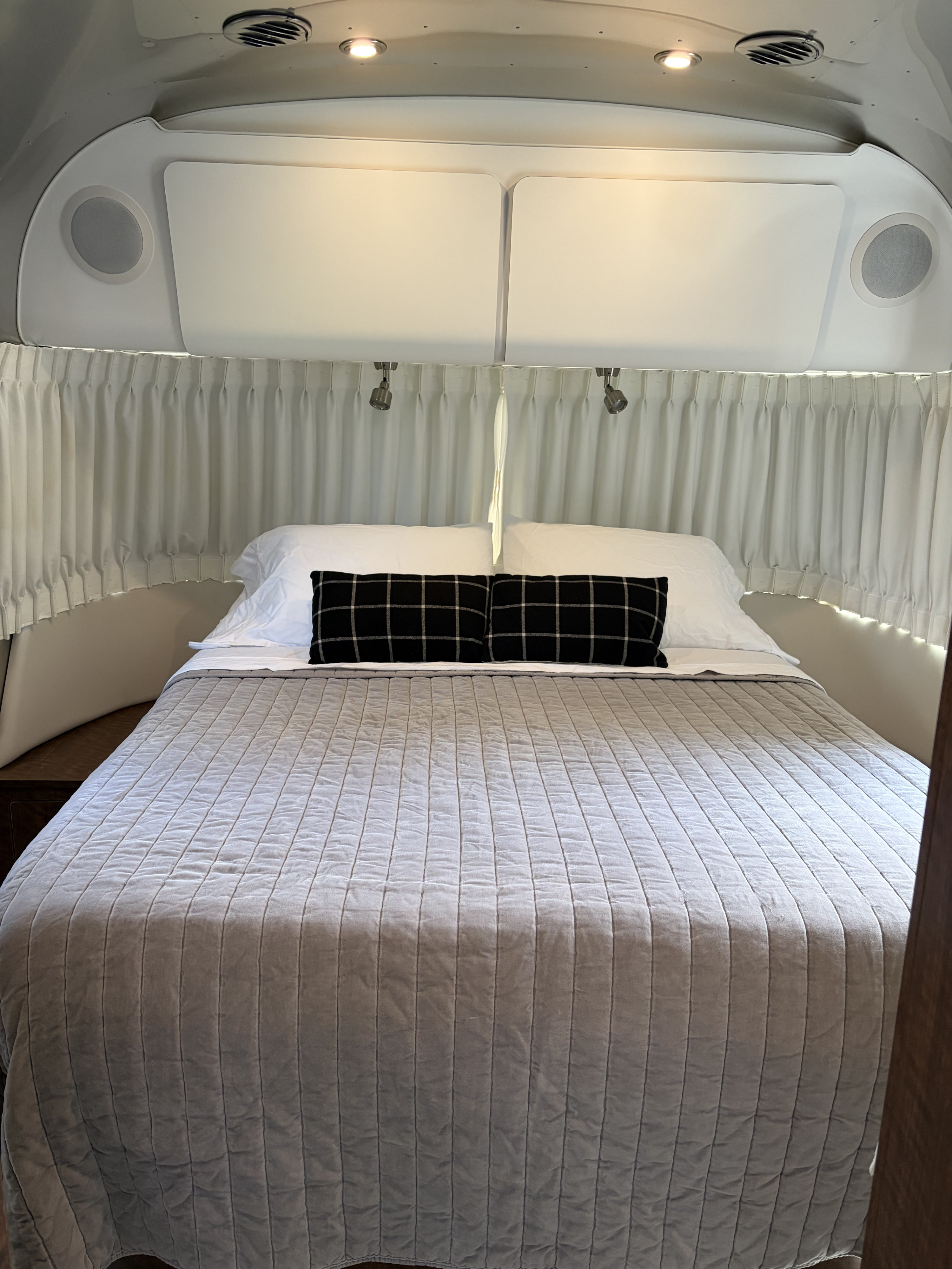 Cozy RV rental bedroom featuring a neatly made bed, modern lighting, and accessible overhead storage for a comfortable stay.. Airstream Globetrotter 2019