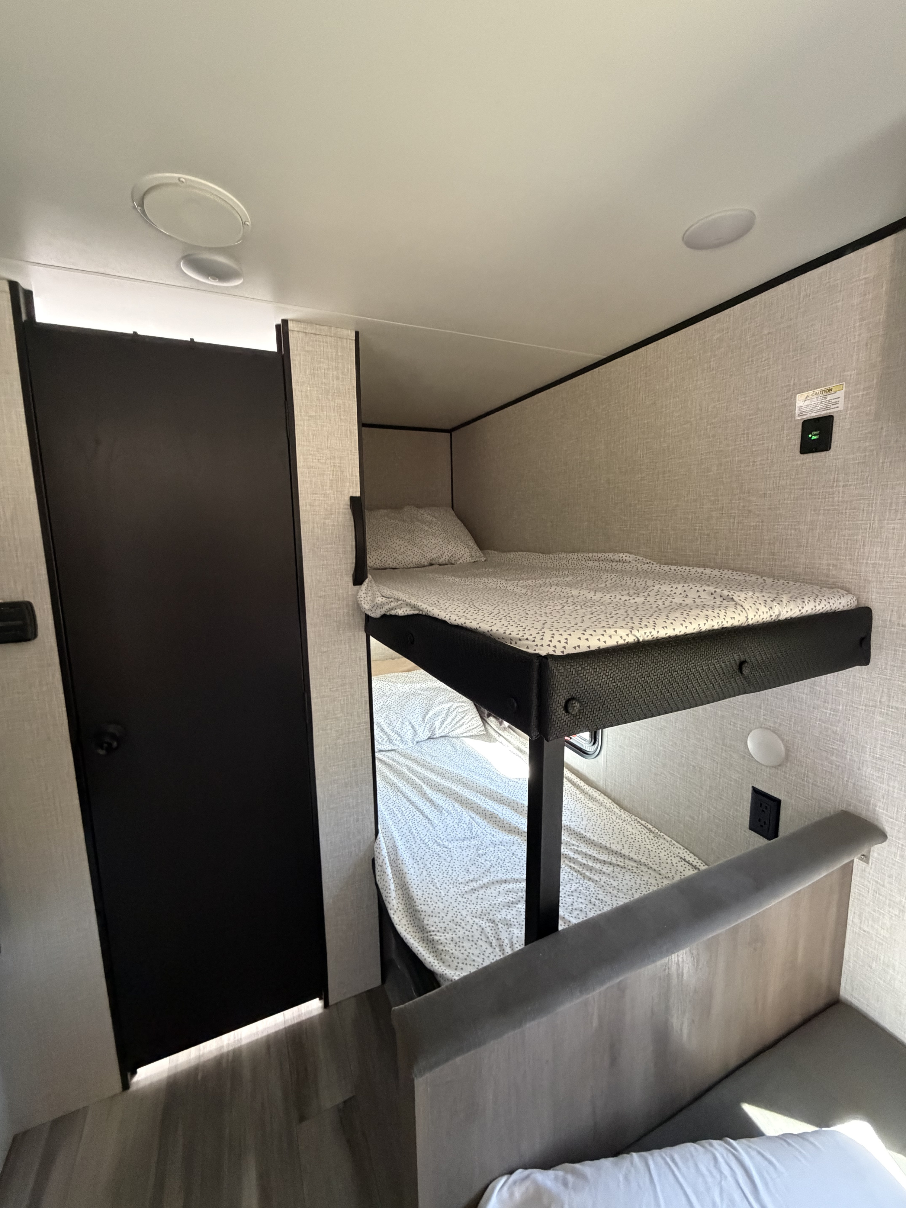 Cozy RV rental bunk beds with patterned sheets, a dark door nearby, and ceiling lights. Ideal sleeping area for family trips.. Jayco Jay Flight SLX Baja Edition 2025