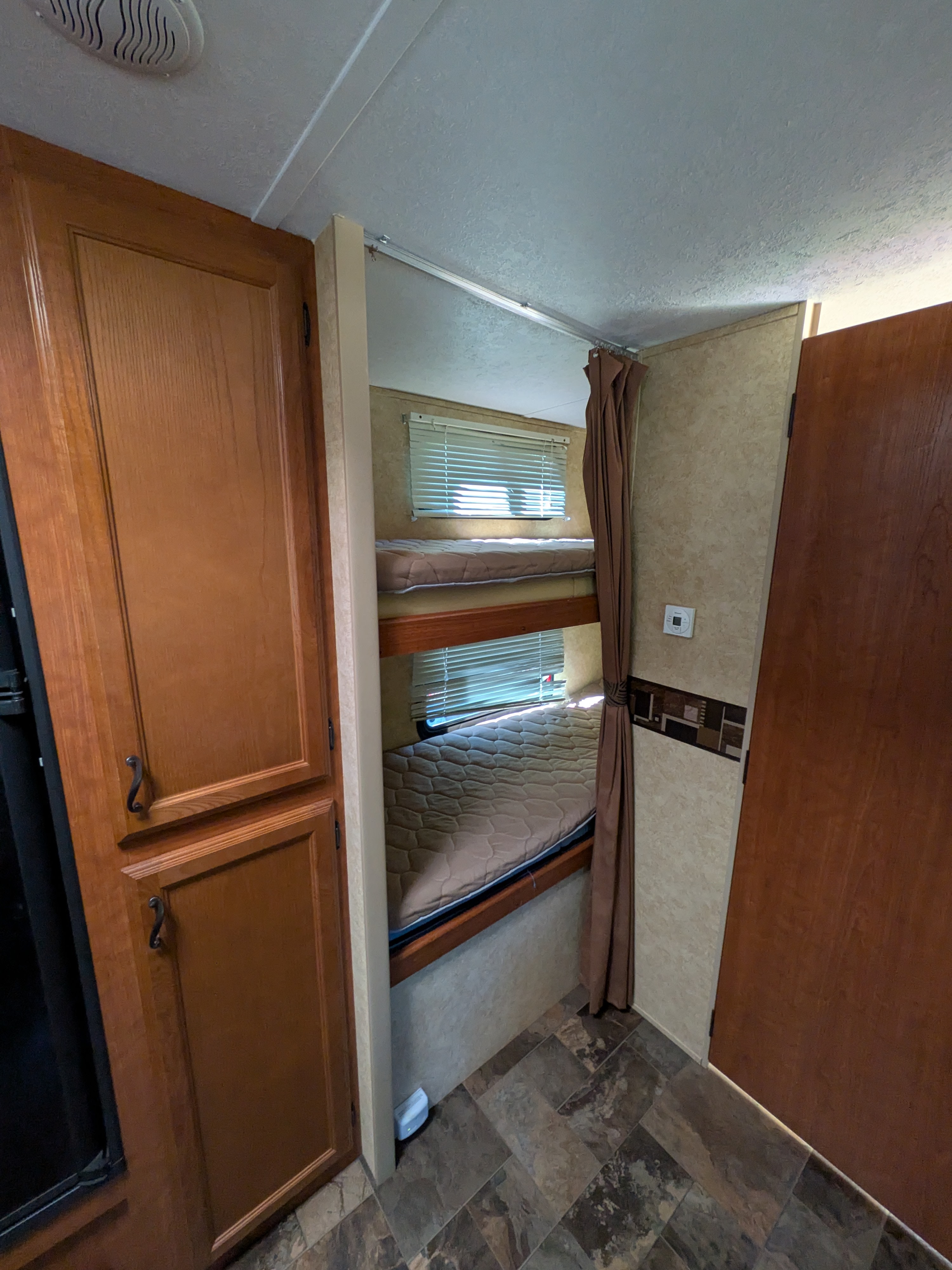 RV rental interior featuring two bunk beds with windows, a privacy curtain, and adjacent wooden storage cabinets.. Forest River Tracer Executive 2012