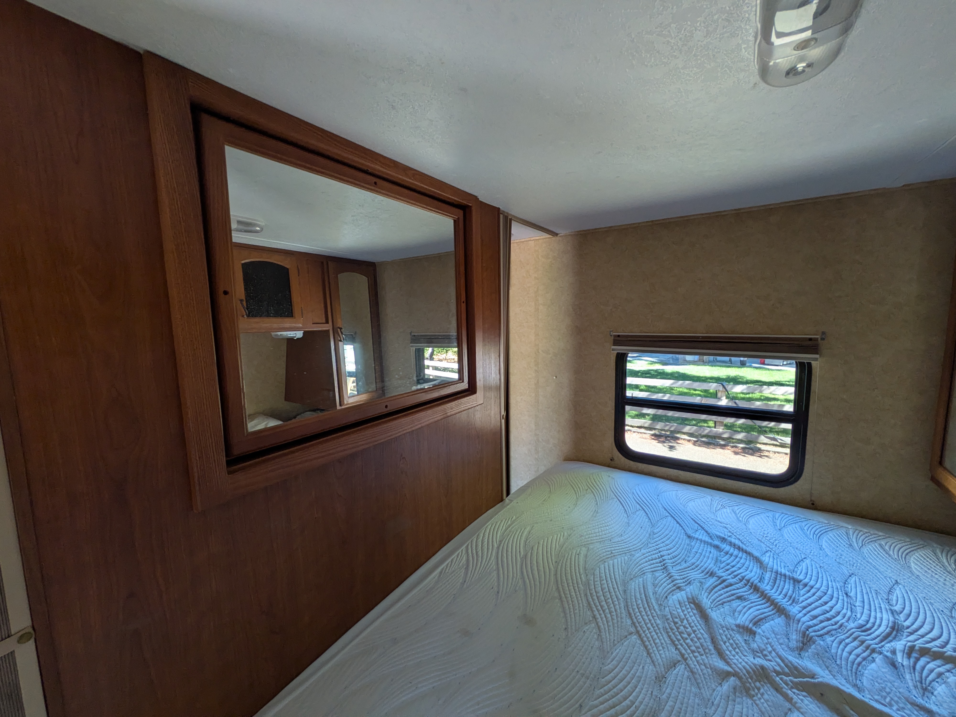 RV rental bedroom interior: bed, large mirror reflecting cabinets, and window with a view.. Forest River Tracer Executive 2012