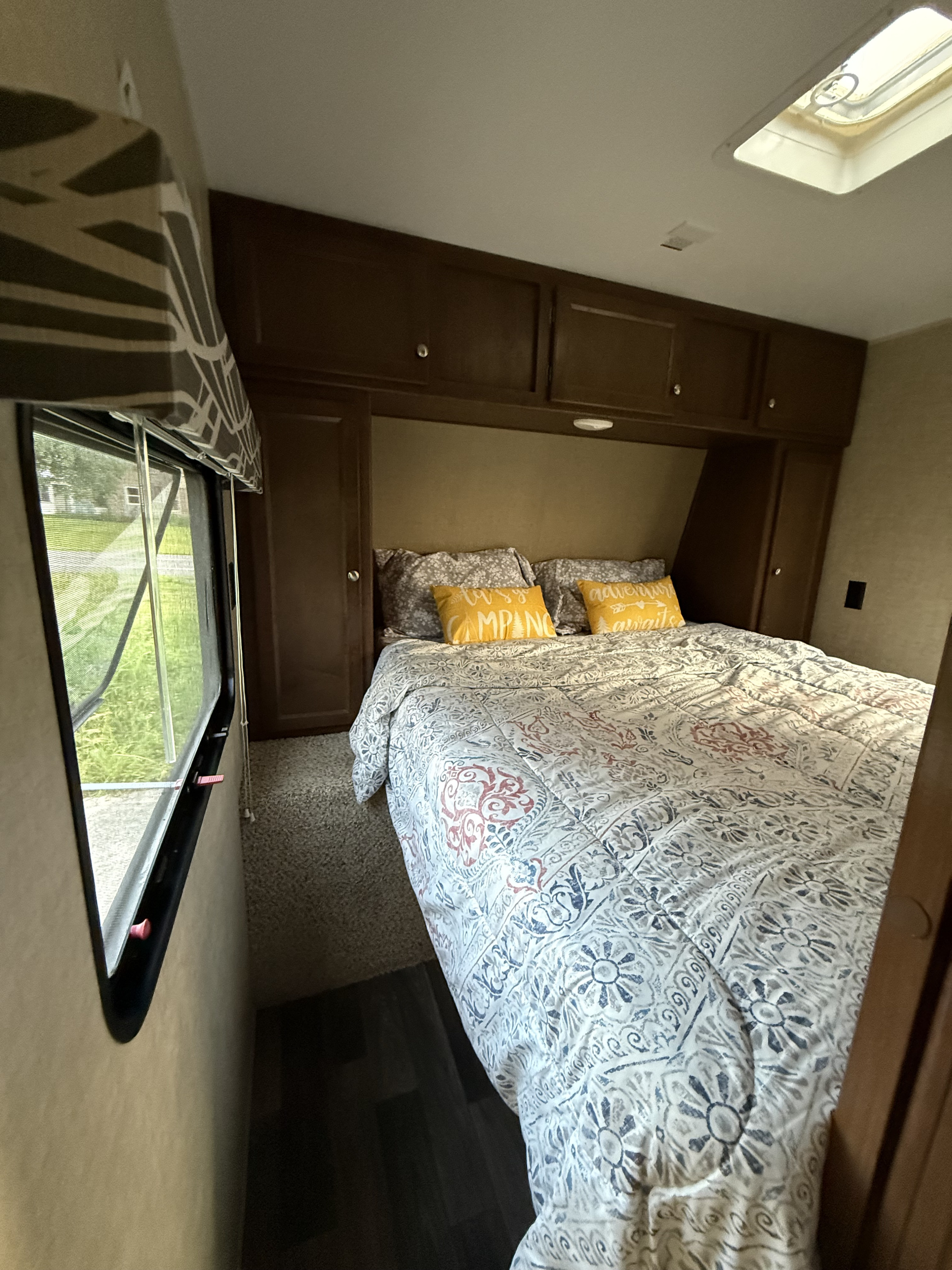 Enjoy a comfortable RV rental bedroom featuring a bed, yellow pillows, overhead cabinets, window view, and skylight.. Keystone RV Hideout Luxury 2017