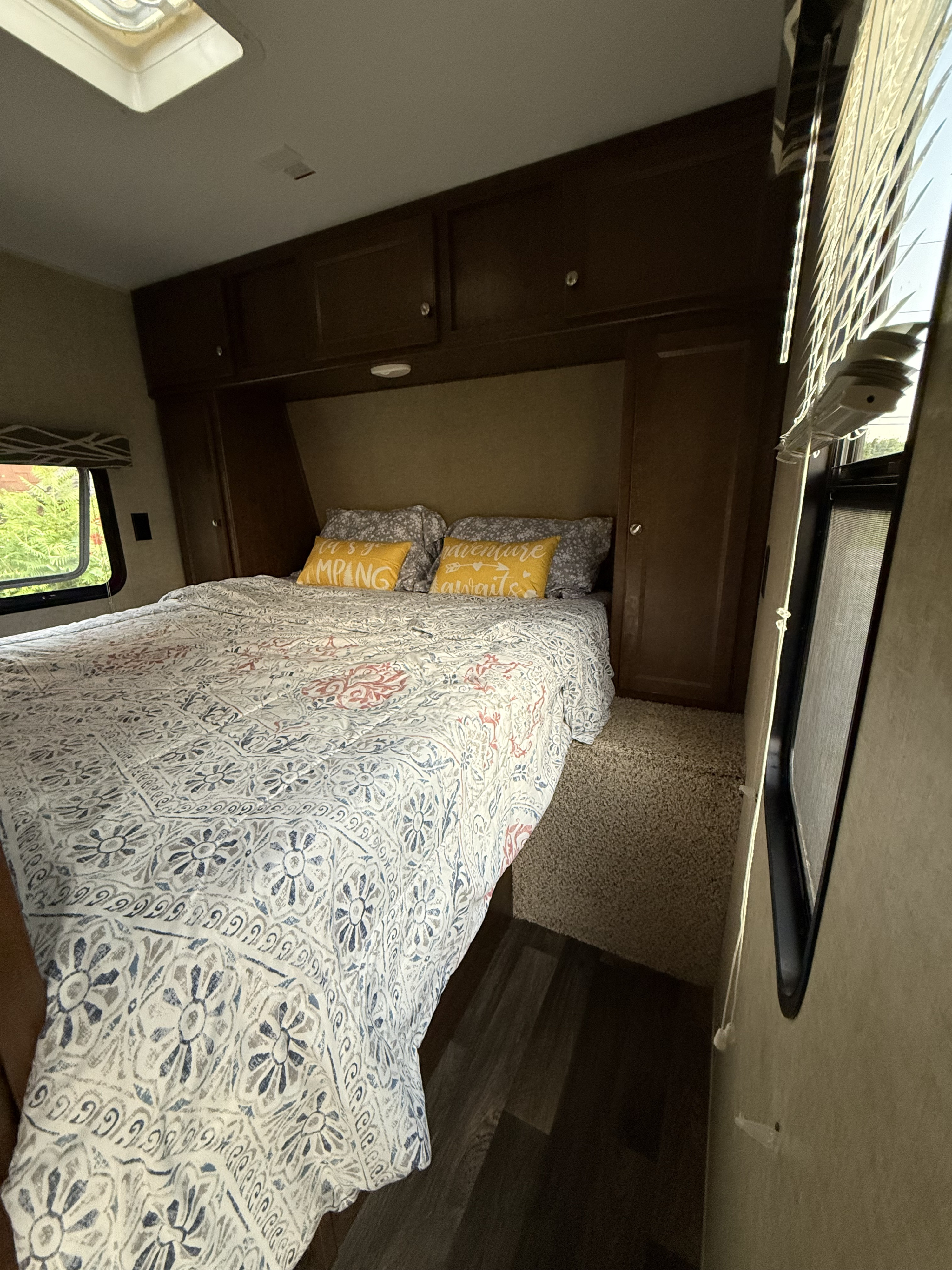 Cozy RV rental bedroom features a patterned bed, "Camping Awaits" pillows, dark wood cabinets, and large windows.. Keystone RV Hideout Luxury 2017