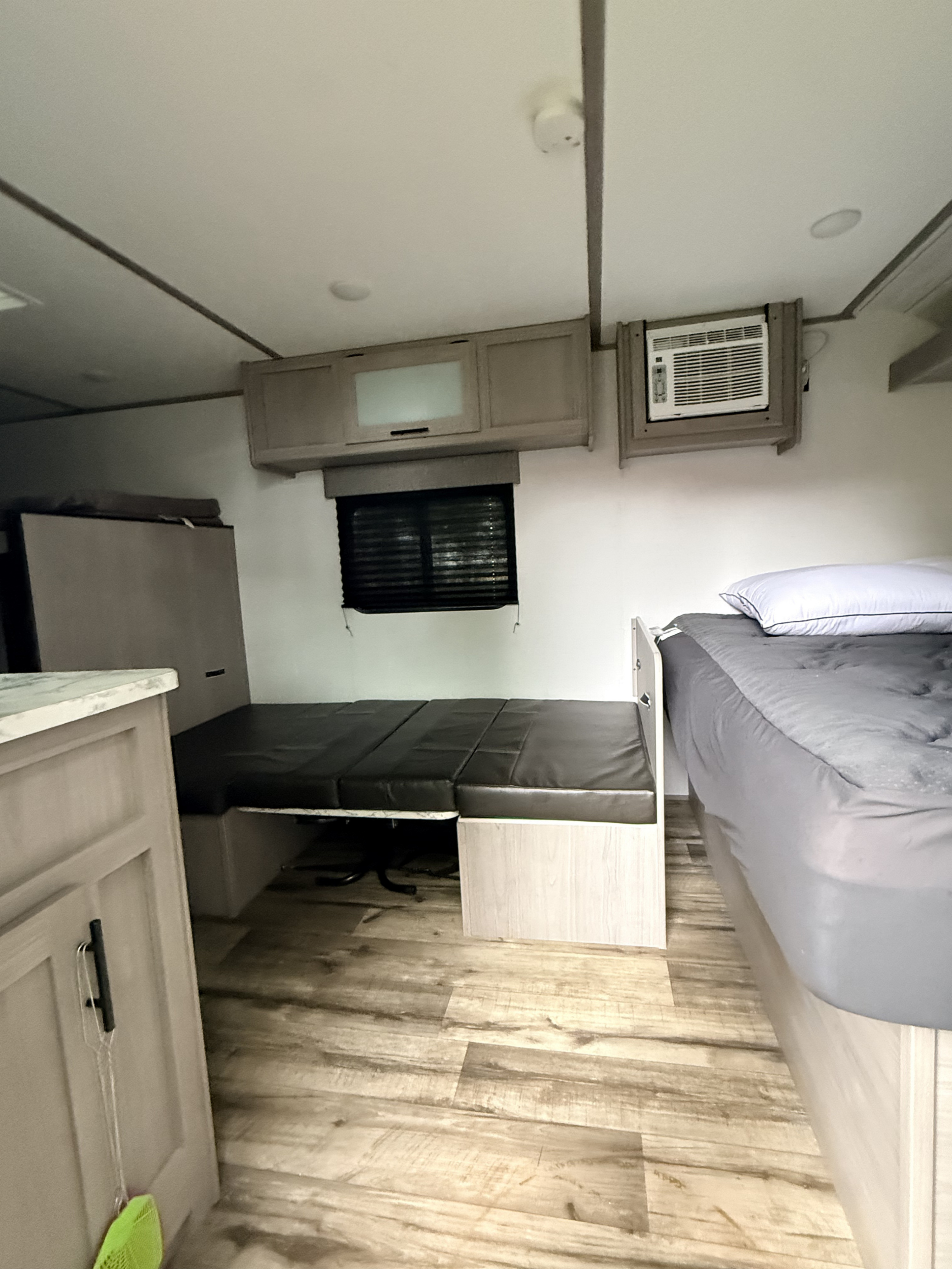 RV rental interior with bed, convertible sofa, wall AC, overhead cabinets, and light wood flooring.. Dutchmen Coleman 2024