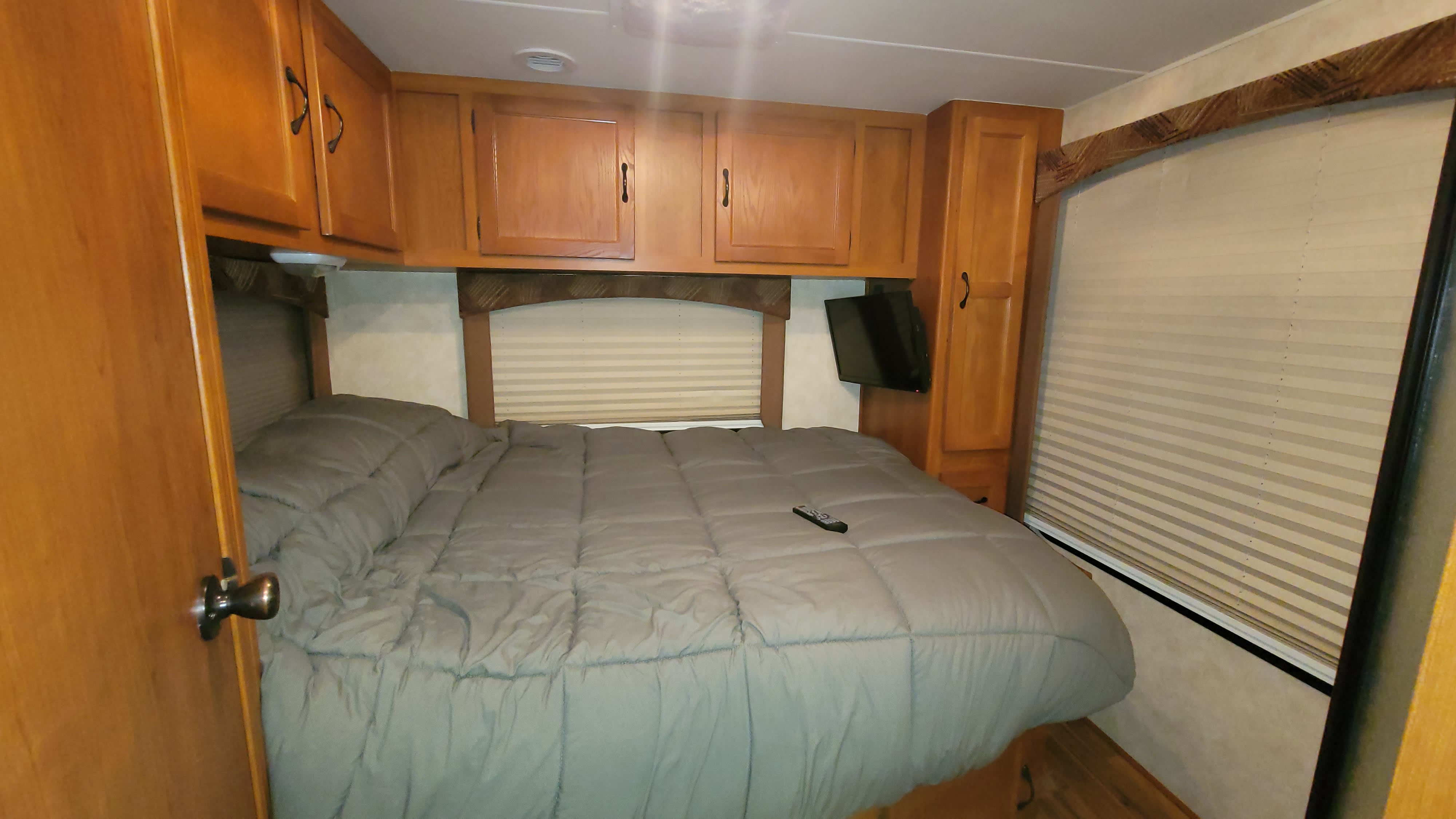 Comfortable RV rental bedroom featuring a cozy bed, overhead wooden cabinets, and a TV, ideal for your next trip.. Forest River Coachmen Freelander 2012