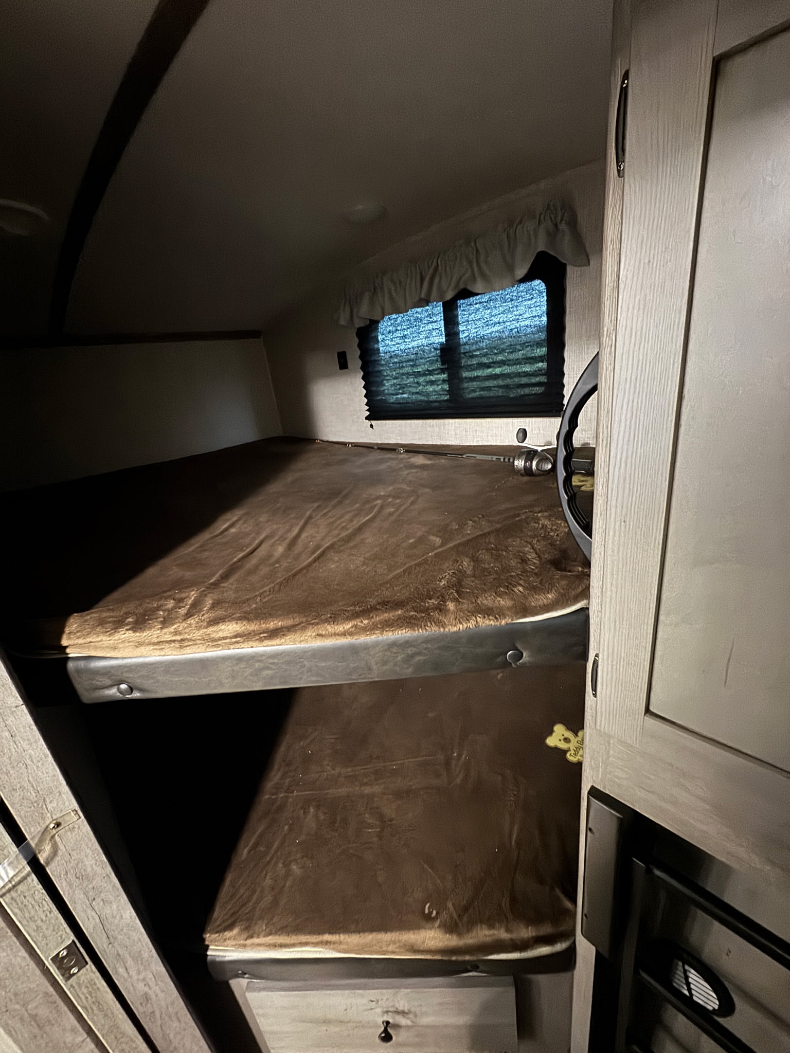 Cozy bunk beds inside an RV rental, with soft brown blankets and a window. A comfortable sleeping area for your next camper adventure.. Keystone RV Outback Ultra-Lite 2020