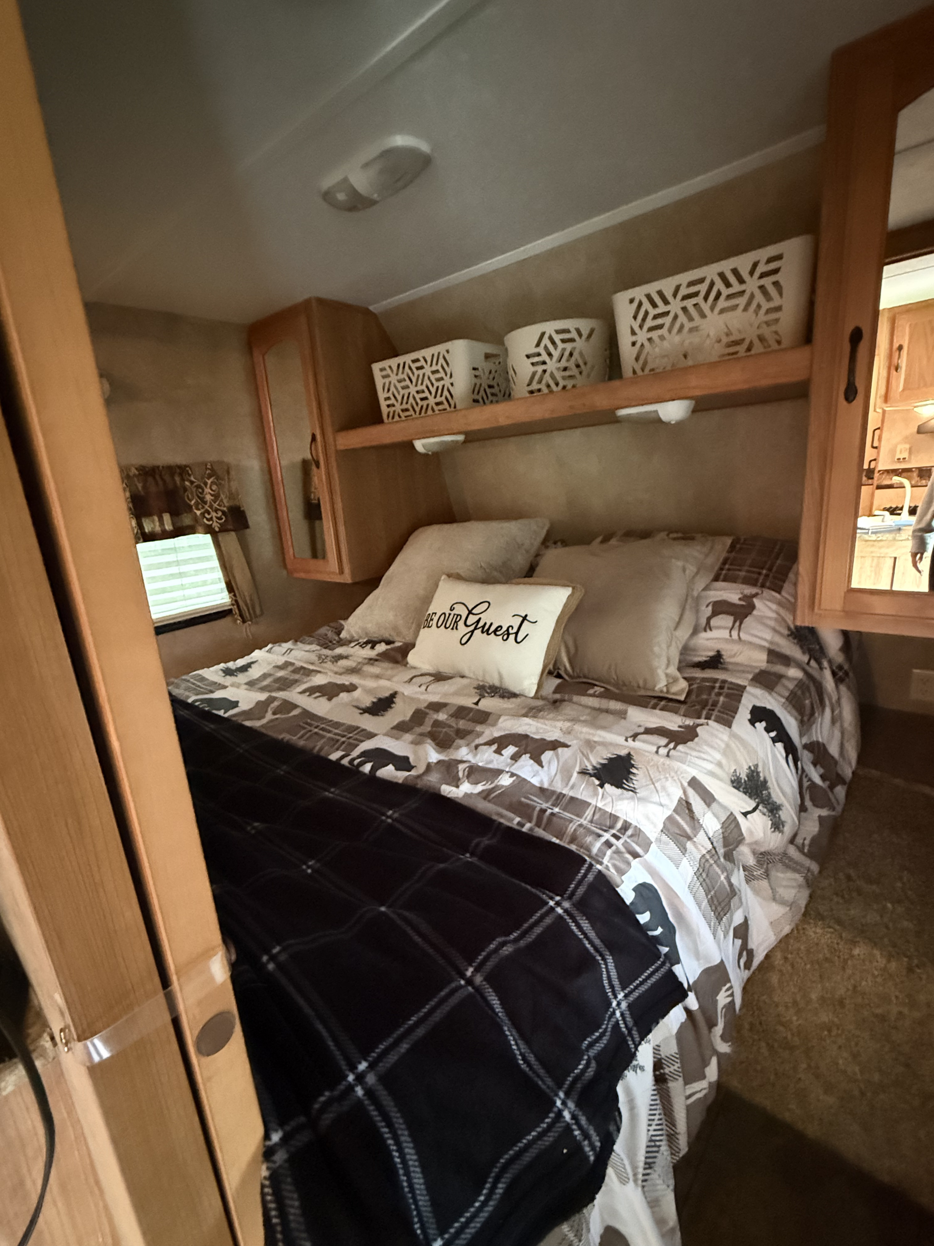 Cozy RV rental bedroom featuring a rustic-themed bed with a "BE OUR GUEST" pillow, overhead storage, and built-in cabinets.. Keystone RV Sprinter Select 2011
