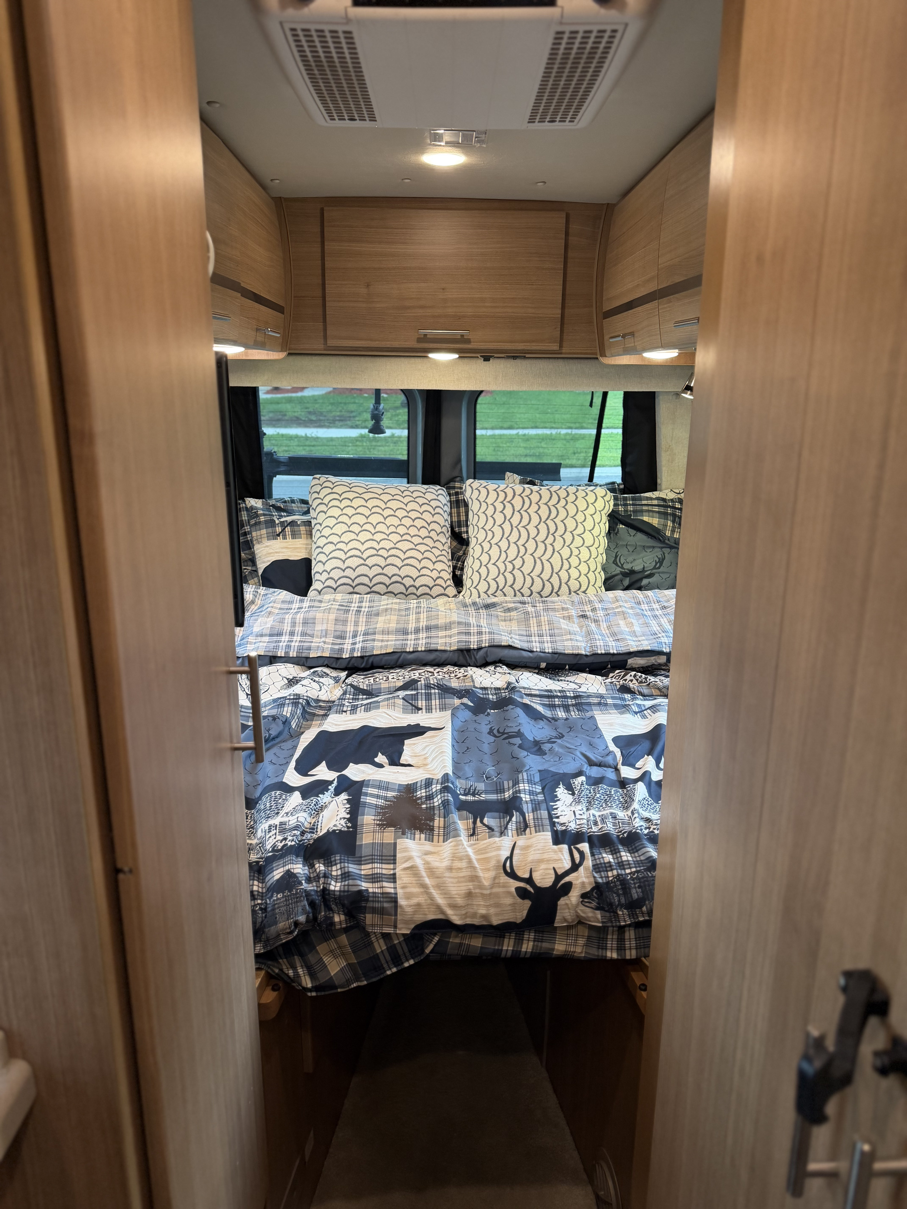 Cozy bed area in an RV rental, featuring rustic bedding, overhead storage, and a view outside, ideal for travel and camping.. ERA ERA Class B 2013